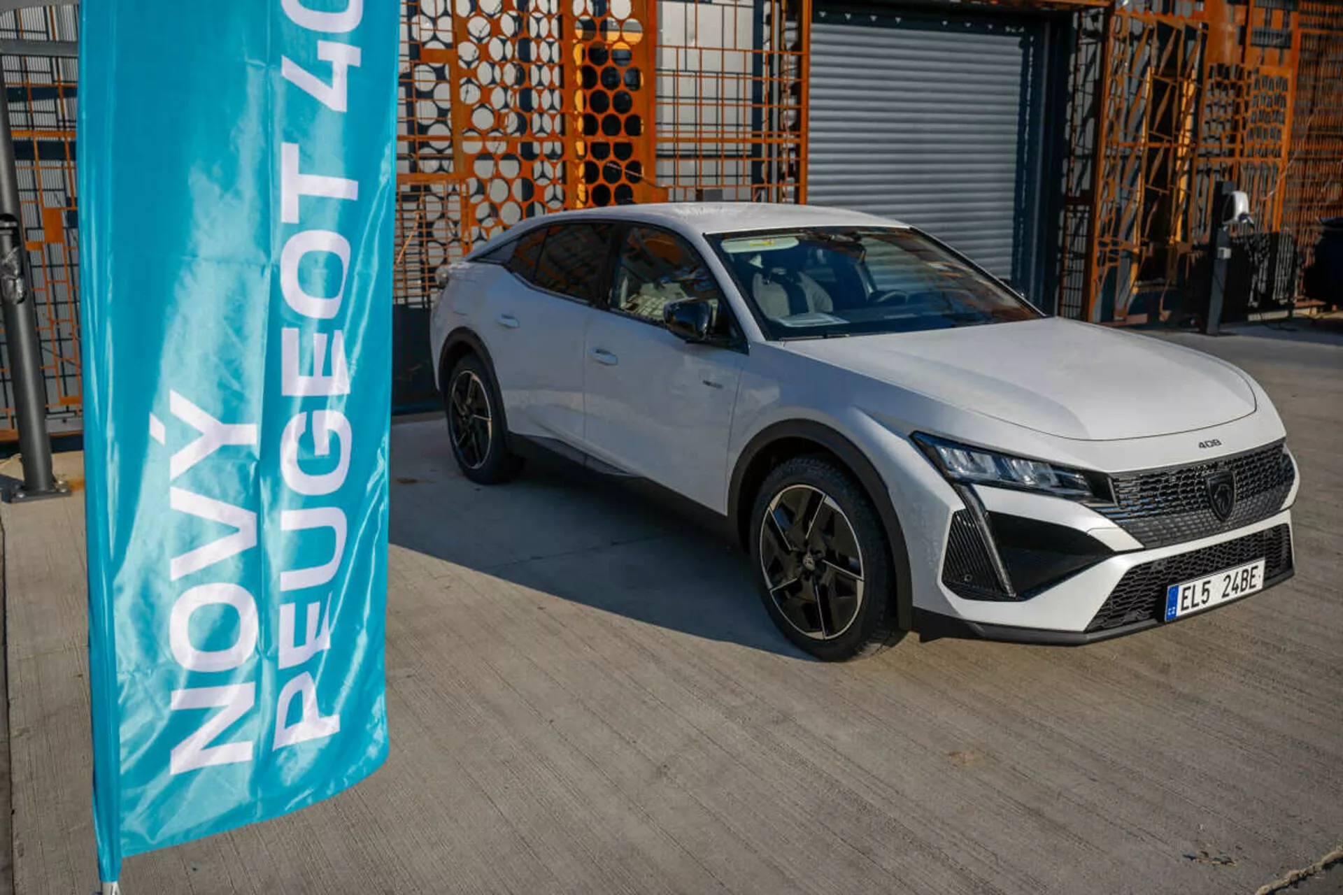Vit Peugeot 408 från 2023 parkerad utomhus med industriell arkitektur i bakgrunden, som visar fordonets design- och teknikfunktioner under naturligt dagsljus