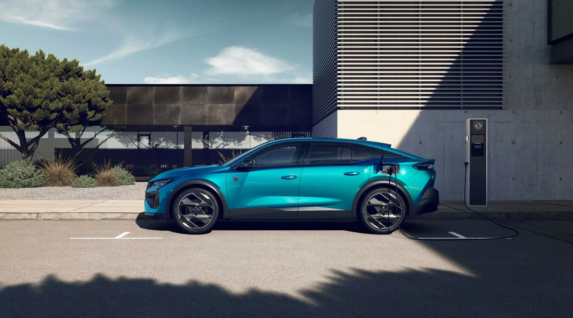 2023 Peugeot 408 elbil i metalliskt blått parkerad vid en utomhusladdningsstation, visar sportiga femekrade legeringshjul, aerodynamisk silhuett, infällda dörrhandtag, synlig laddningsport, konventionella sidospeglar, tonade rutor för integritet och panoramasoltak under ljusa dagsljusförhållanden med modern arkitektur i bakgrunden