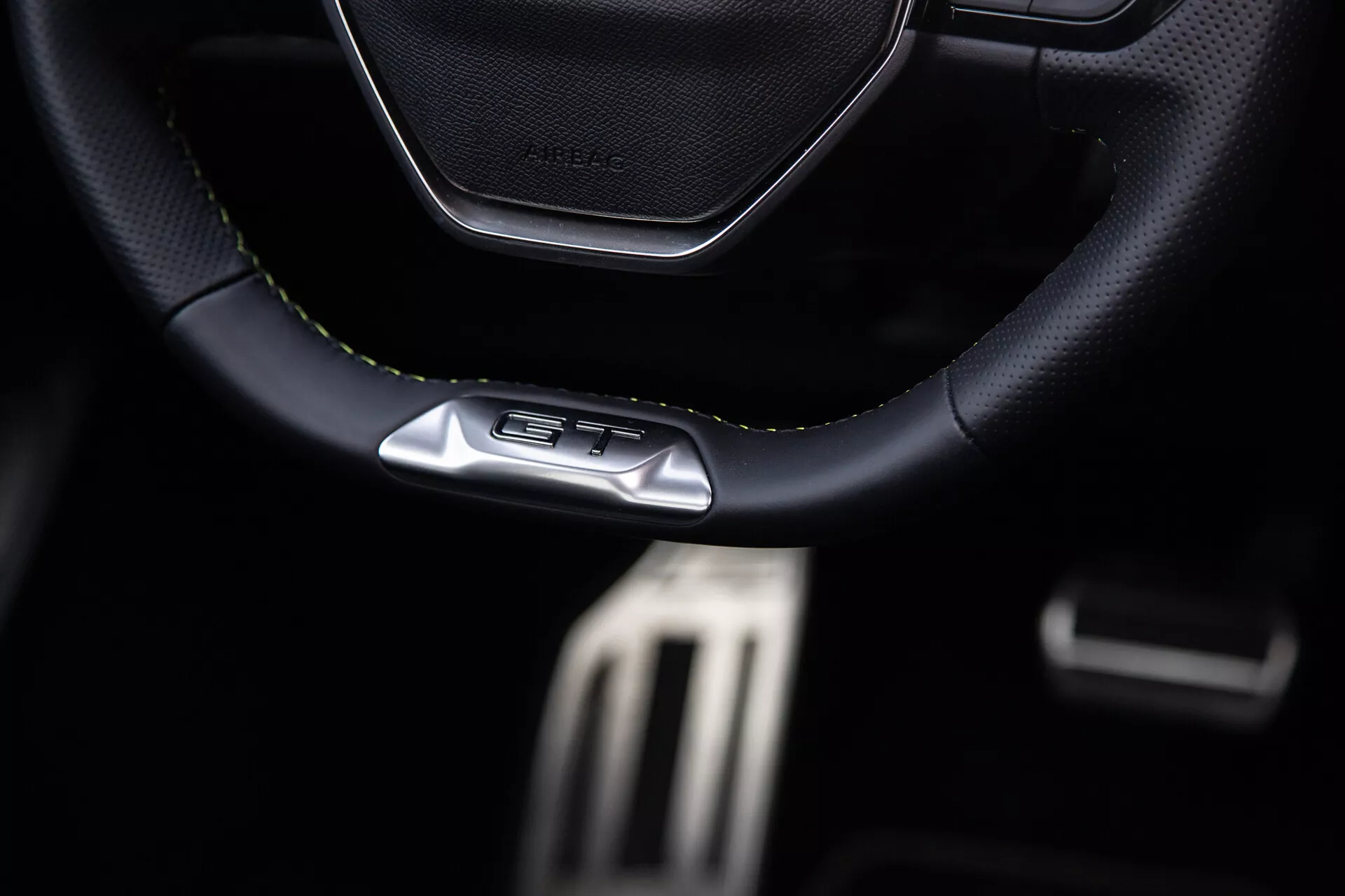 Interiör av Peugeot 408 2023 med fokus på sportigt lädernäht ratt med GT-emblem, metalliska prestandapedaler och premium mörka cockpitfunktioner