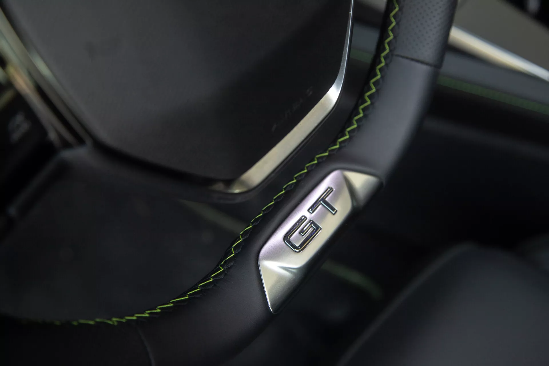 Närbild av ratten och instrumentbrädan i Peugeot 408 2023, med en svart läderratt med grön söm och en GT-emblem, som framhäver lyx och sportighet