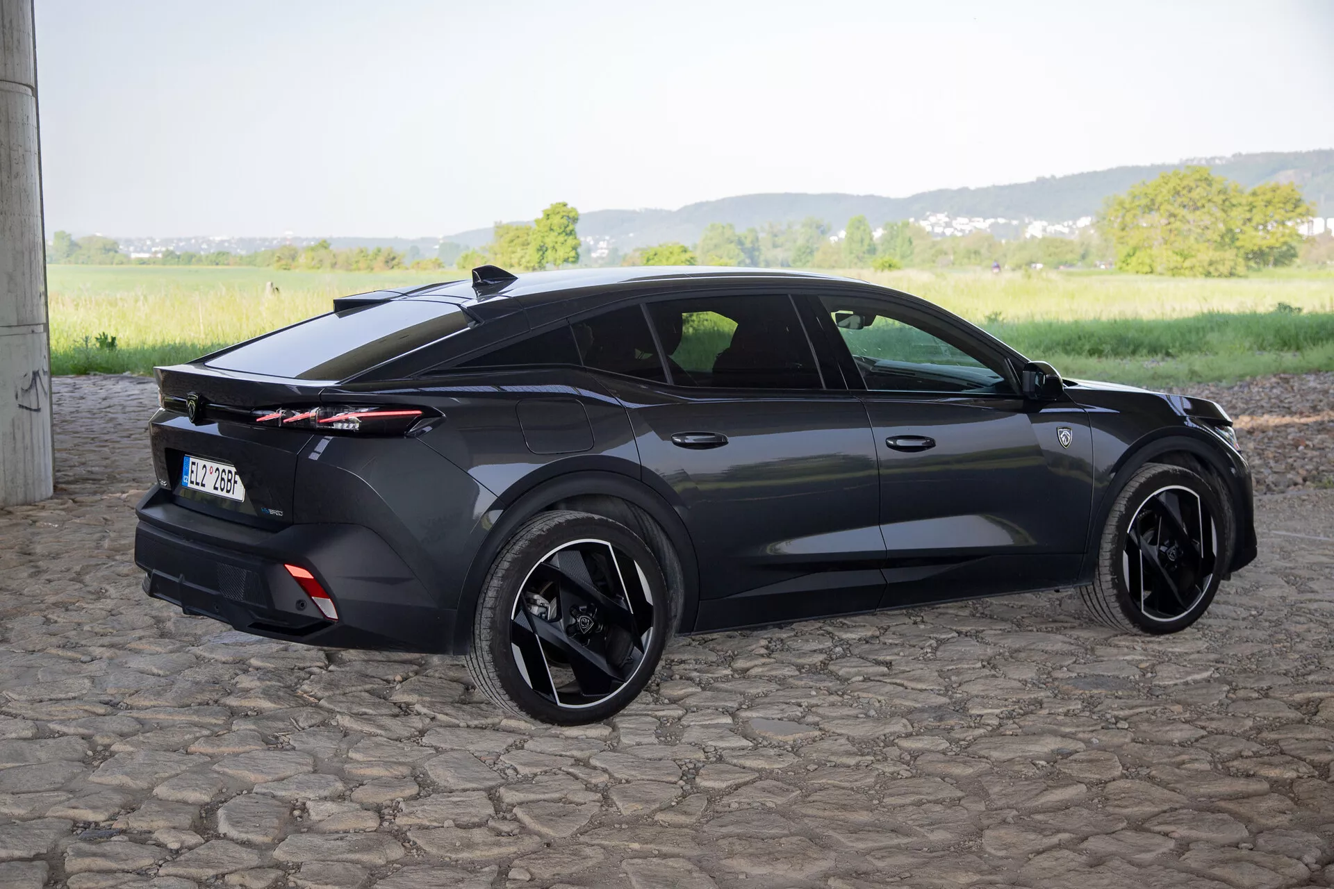 Peugeot 408 från 2023 fångad från ett bakre tre fjärdedels vinkel som framhäver dess sportiga hatchbackdesign, integrerad bakspoiler med fullängds bakljus, svarta legeringshjul och samtida funktioner som infällda dörrhandtag och sidospeglar med blinkers, i naturligt dagsljus