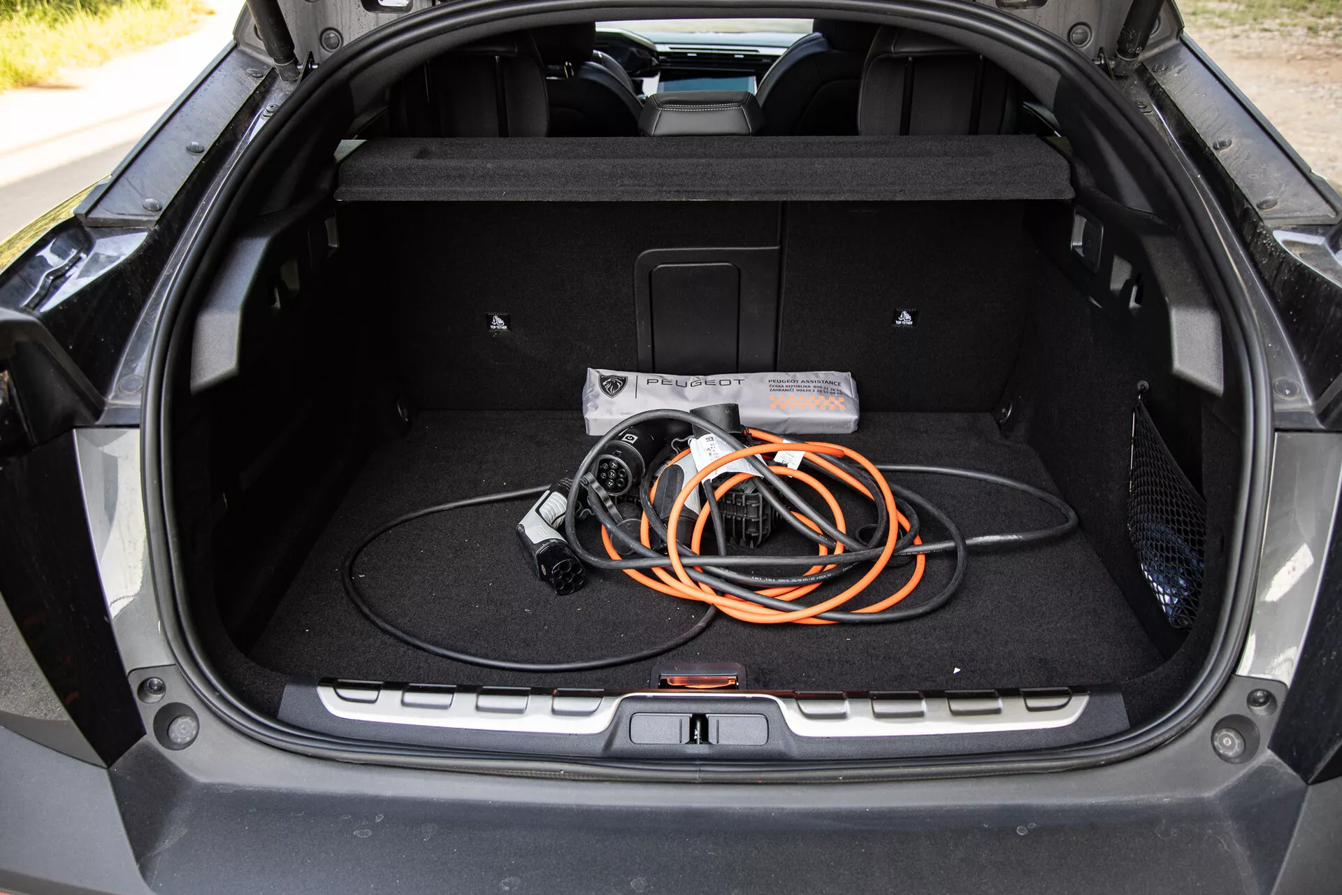 Interiörvy av bagageutrymmet i Peugeot 408 2023 som visar en rymlig design och en laddningskabel för elbilar, framhäver EV-teknik och modern byggkvalitet.