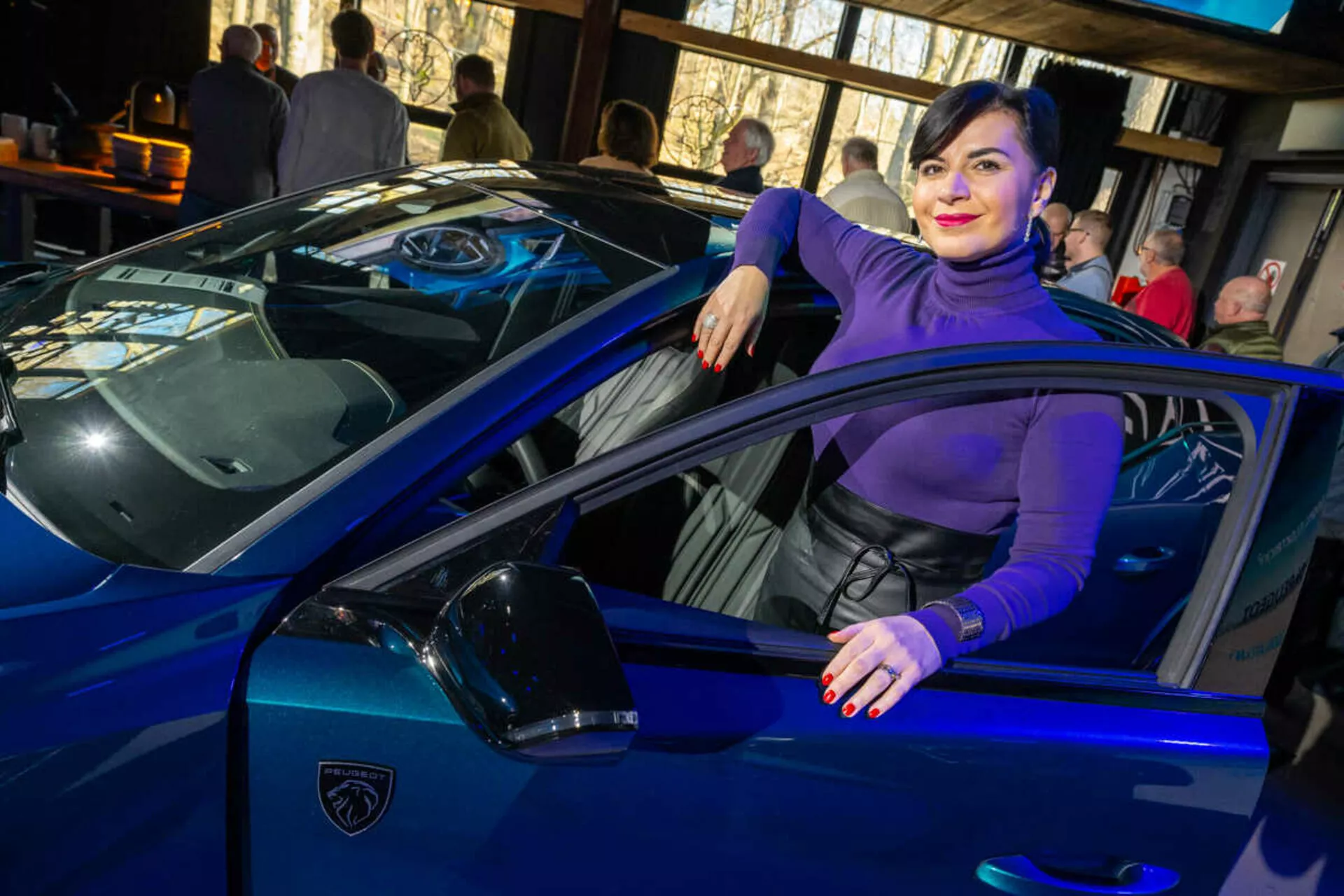 Livligt blå sportbil, möjligtvis en Lamborghini, fångad från en tredjedels vinkel som betonar dess slanka linjer, skarpa LED-strålkastare och ikoniska sköldformade logotyp, med en person som avslappnat interagerar med fordonet vilket antyder lyx och stil.