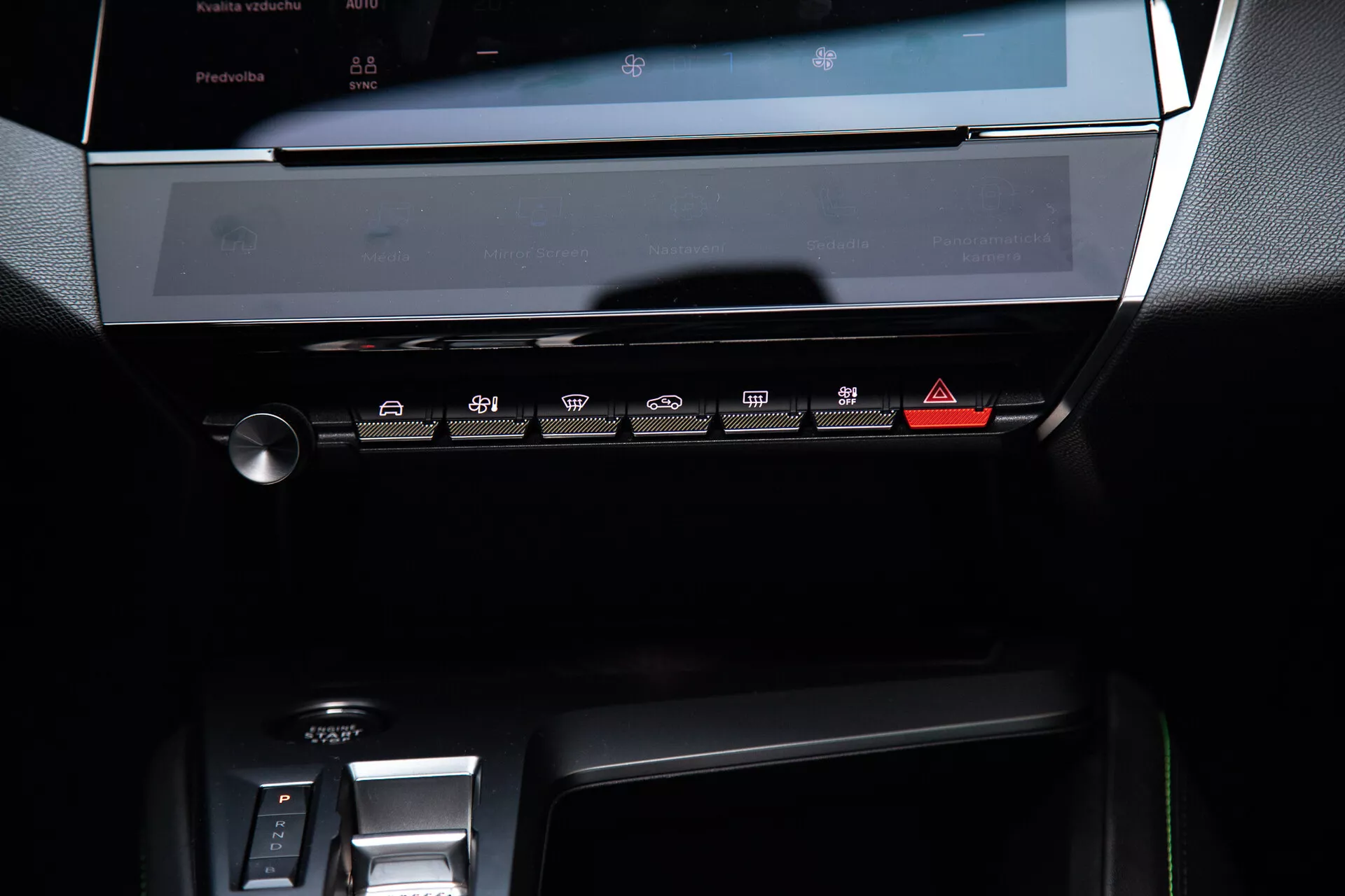 Central instrumentbräda i en Peugeot 408 från 2023 som visar det avstängda pekskärmssystemet för underhållning, klimatkontrollpanelen med beröringskänsliga knappar och en del av området för den elektroniska växelspaken, belyst med mjukt omgivningsljus som framhäver dess moderna, eleganta design med mörka toner och metalliska accenter.
