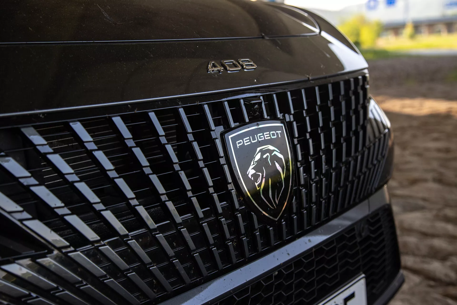 Detaljerad vy av Peugeot 408 2023 frontgrill som visar det intrikata mönstret och silverlejonlogotypen, under naturligt ljus