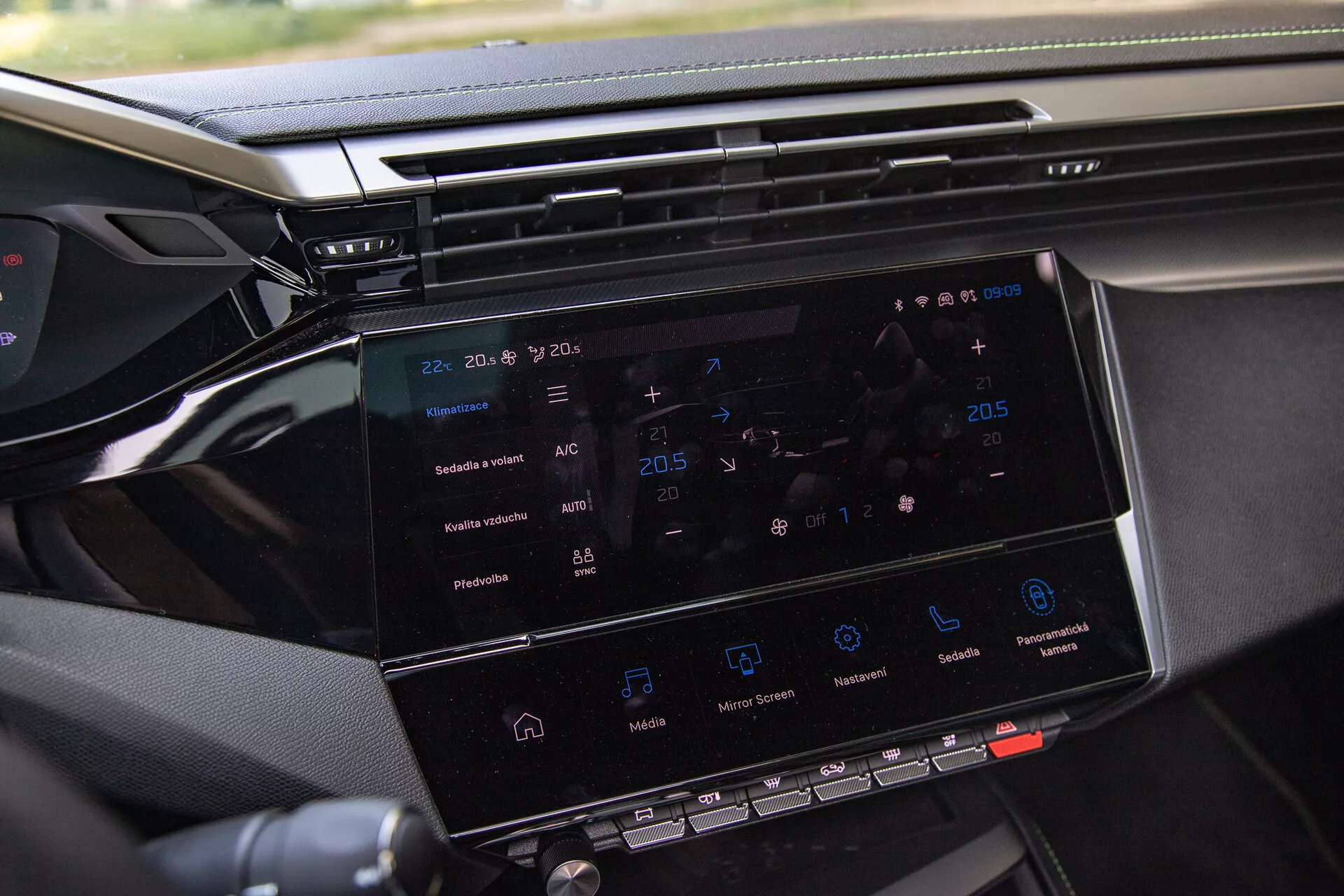 Närbild av Peugeot 408 2023 underhållningssystem som visar 8-10 tums pekskärm med navigering, klimatkontroll, mediaspelningsikoner och en glimt av instrumentbrädan, taget från passagerarsidan
