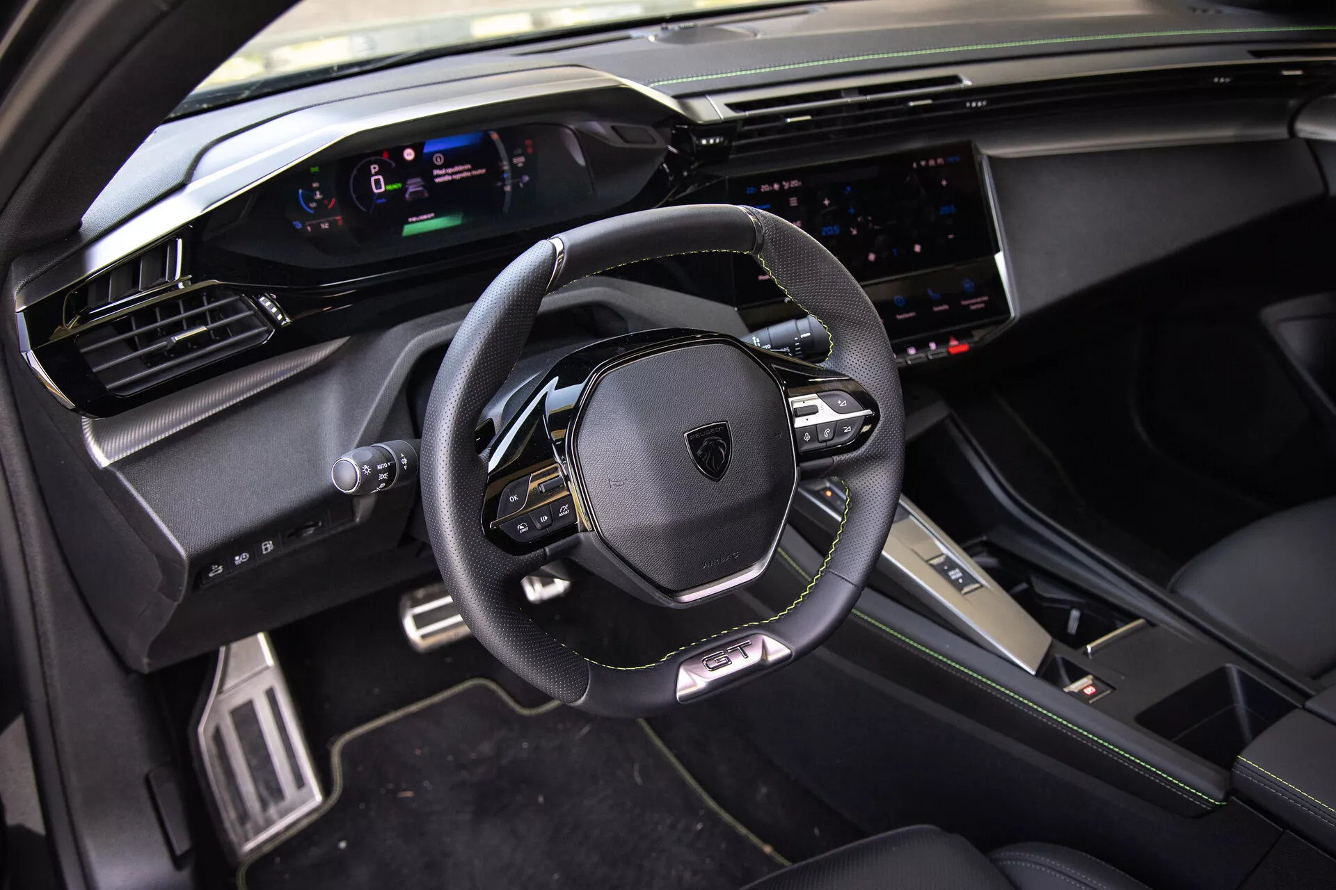 Interiören i Peugeot 408 2023 som visar en läderomsluten, multifunktionell ratt, en digital instrumentpanel, ett brett pekskärmsinfotainmentsystem och sportiga, premium designelement i naturligt dagsljus från främre passagerarens perspektiv.