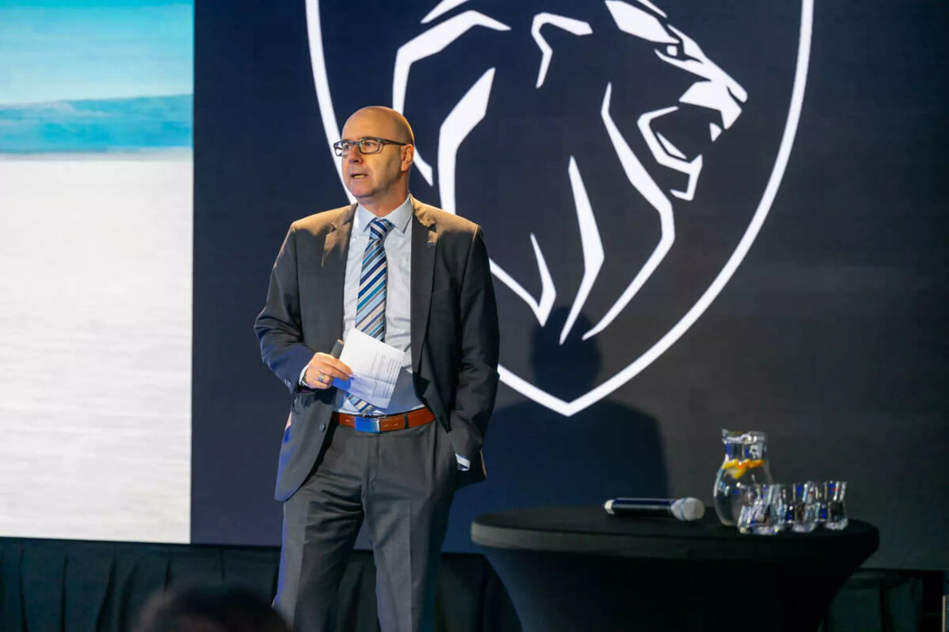 Professionell talare som presenterar framför en bakgrund med en tigerhuvudlogo, eventuellt representerande ett varumärke, ingen Peugeot 408 eller någon bil synlig