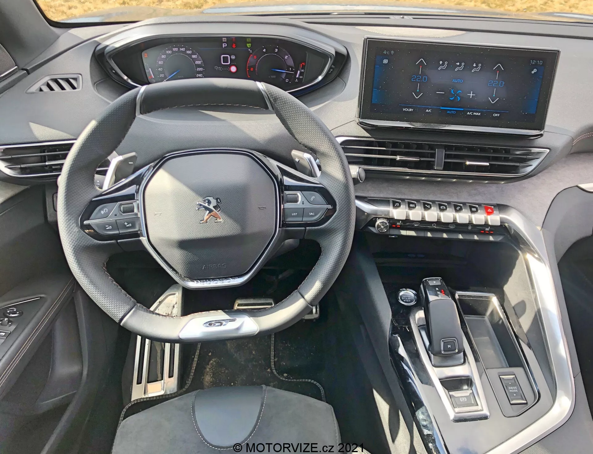 Interiörvy av en Peugeot 5008 från 2021 från förarsätet, med sportig multifunktionsratt med monterade kontroller, delvis digital instrumentpanel, en stor pekskärmsinfotainmentsystem, taktila klimatkontrollknappar, elegant växelväljare och moderna designelement med metalliska accenter för en högteknologisk, lyxig upplevelse.