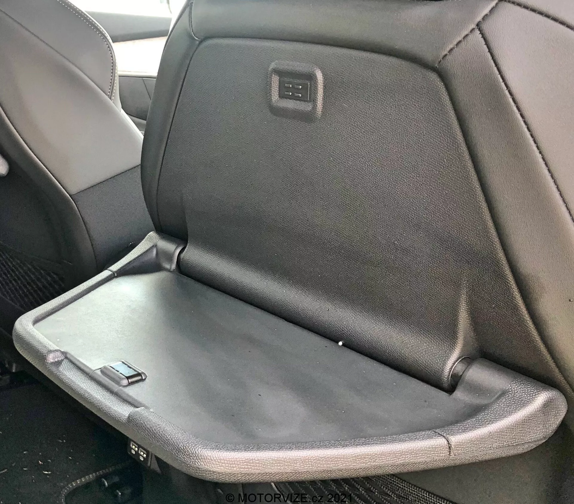 Interiörvy av en Peugeot 5008 2021 med ett baksäte som har ett fällbart armstöd eller brickbord, som visar en blandning av tyg- och läderklädsel med en integrerad skärm eller kontrollpanel på baksidan av framsätets nackstöd.