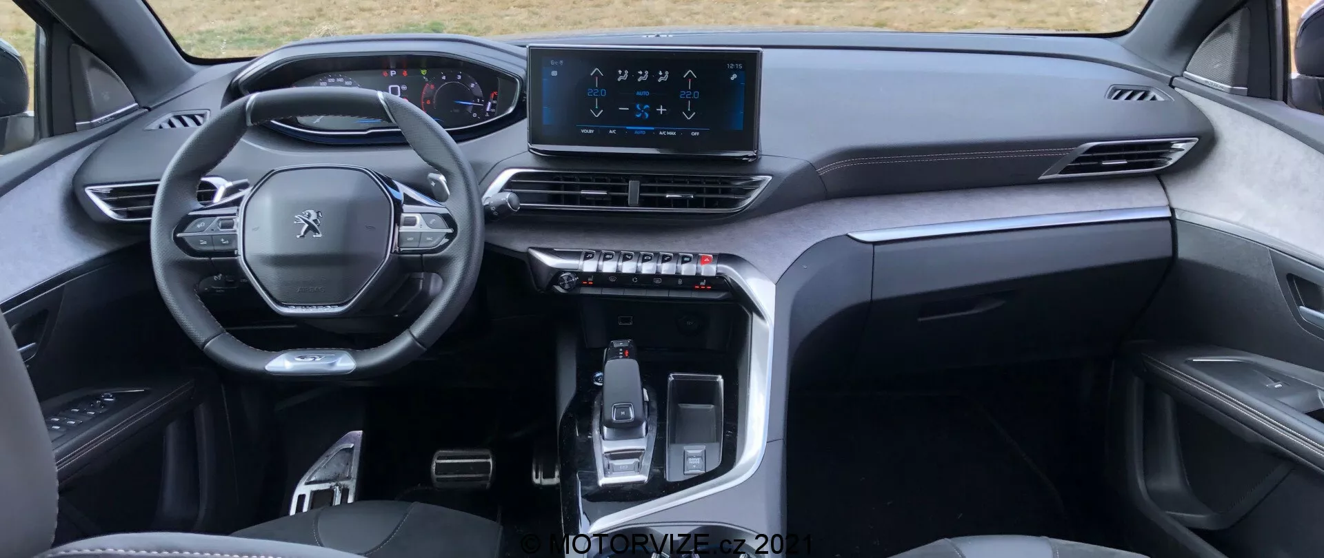 Interiörvy av en Peugeot 5008 2021 från baksätets perspektiv, med fokus på en multifunktionell ratt, digital instrumentpanel, symmetrisk instrumentbräda med luftventiler, central infotainment pekskärm och en elegant mittkonsol med elektroniskt styrd växelspak och beröringskänsliga knappar. Den stiliga, minimalistiska designen använder högkvalitativa material, vilket antyder ett modernt premiumfordon.