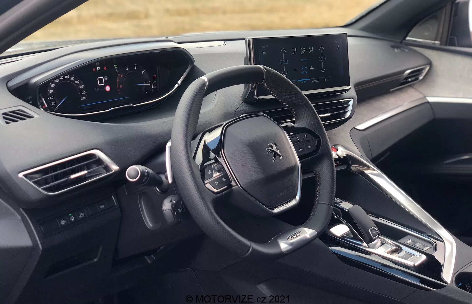 Interiörvy av Peugeot 5008 2021 från förarens perspektiv, som visar ratten med Peugeot-logotypen, flera kontrollknappar, fullt digitalt instrumentkluster, central infotainmentskärm med navigationskarta, elegant instrumentpanel med minimala fysiska knappar, mittkonsol med knappar för klimatkontroll och fordonsinställningar, elektronisk växelspak, luftventiler, start/stopp-knapp för motorn, material av hög kvalitet och delvis vy av förarsätets nackstöd.