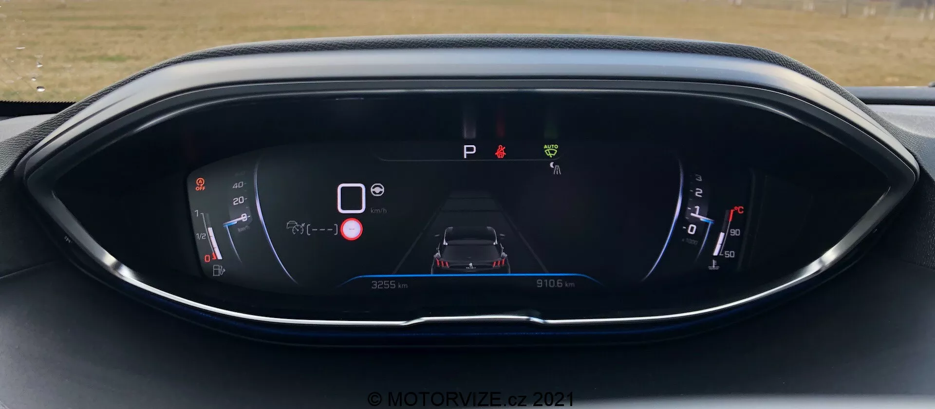 Instrumentbräda på Peugeot 5008 2021, som visar en digital display från förarsätets perspektiv. Displayen innehåller en ström-/batterimätare, en central bilgrafik med varningsikoner, en 'P'-indikator för parkering, en bränslemätare och information om tripmätare. Designen har ett modernt blått och rött färgschema på ett elegant, böjt hölje. Vattenstämpel © MOTOR1ZED 2021.