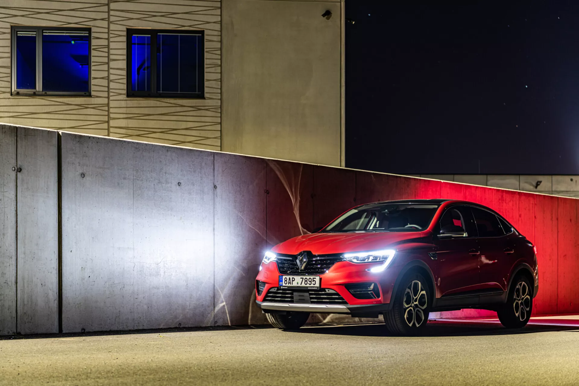 Sportig halvkombi Renault Arkana 2021 parkerad på natten, som visar upp LED-strålkastare, frontgrill och legeringshjul under konstgjord belysning