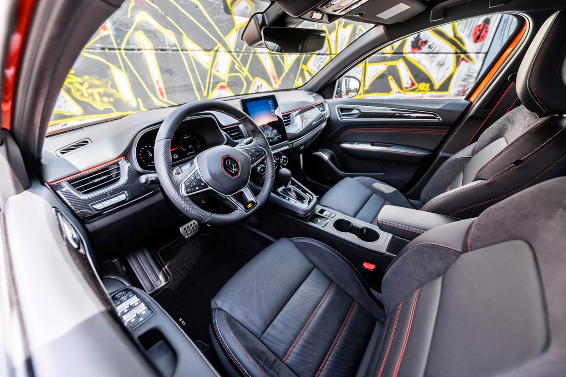 Interiörvy från passagerarsidan av Renault Arkana 2021 med ratt med media- och farthållarkontroller, digital instrumentbräda, infotainmentsystem, automatisk växellåda, sportiga säten med lyxdetaljer och avancerade tekniska funktioner