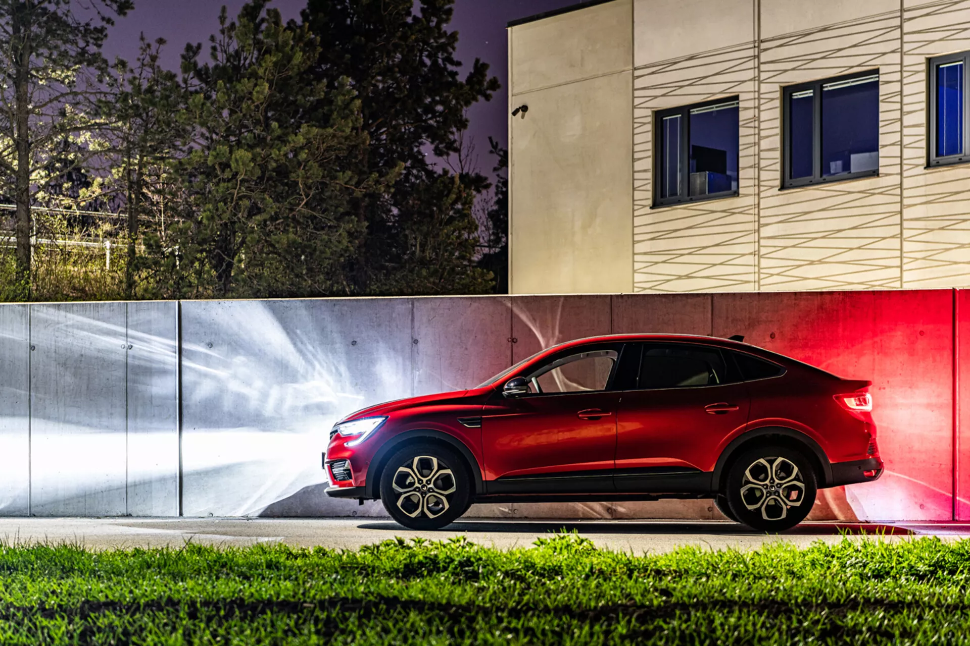 Sidoprofilvy av Renault Arkana 2021 på natten, som framhäver dess eleganta röda färg, sportig design och avancerade funktioner mot en stiliserad stadsbakgrund