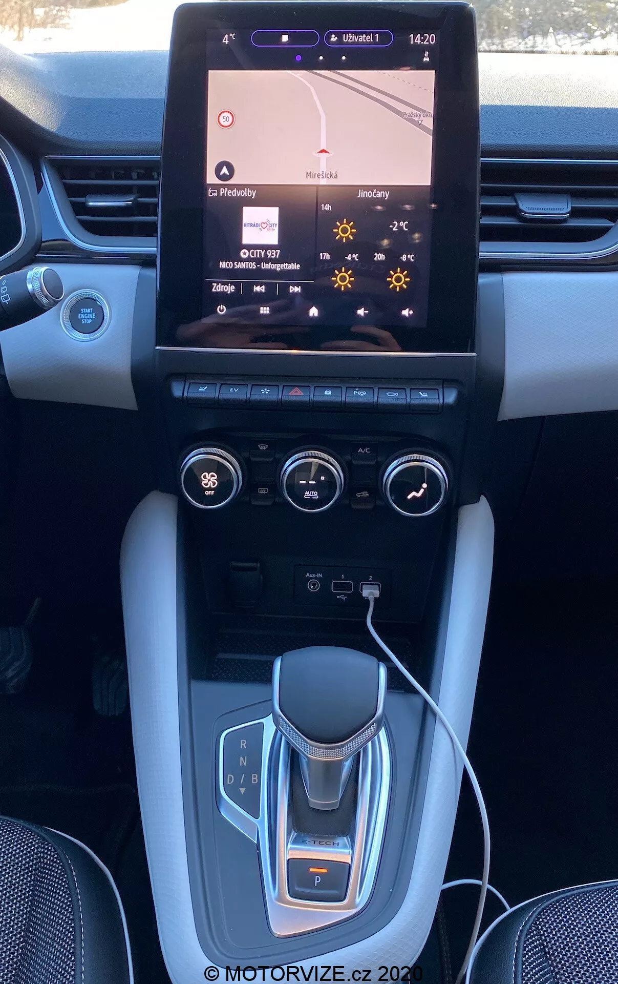 Interiör av Renault Captur 2020 som visar mittkonsol och instrumentbräda med ett stort pekskärmsinformationssystem som visar navigationskartan, tvåzons klimatkontroller, elektronisk växelväljare, mugghållare, borstade metalldetaljer och eventuella lyxiga ytor.