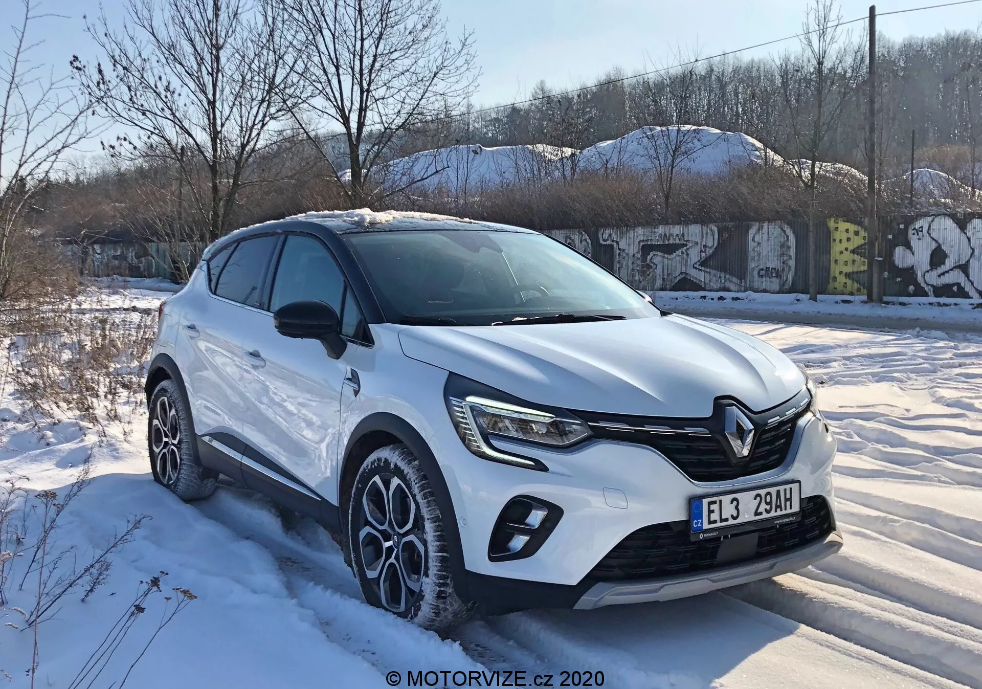 2020 Renault Captur sett från trekvarts framsida som visar modern crossover-design med distinkt frontgrill, skarpa LED-strålkastare, karossöverdrag, stora mulltispokade lättmetallfälgar och vit karossfärg under snöiga vinterförhållanden i en urban miljö.