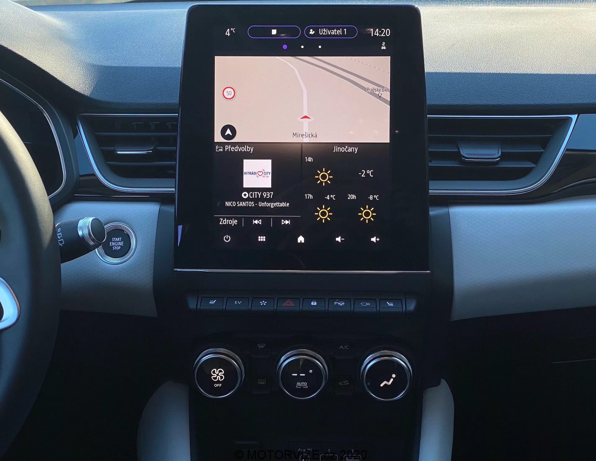 Bilden visar mittkonsolen på en 2020 Renault Captur från förarplatsens perspektiv. Huvudfunktion är en vertikalt orienterad pekskärm för infotainment som visar navigation, tid (14:20), temperatur (27°C) och radioinformation. Nedanför finns ett tvåzoners klimatanläggningssystem med vred och knappar som visar inställningar som 'Hi' för förarsidans temperatur. Konsolen kombinerar metall- och plastmaterial kring skärmen och kontrollerna. Instrumentpanelens kanter avslöjar en tvåtons mjuk design och en Start/Stop-knapp är delvis synlig. Ratten och en styrspak syns, troligtvis för blinkers eller andra funktioner.