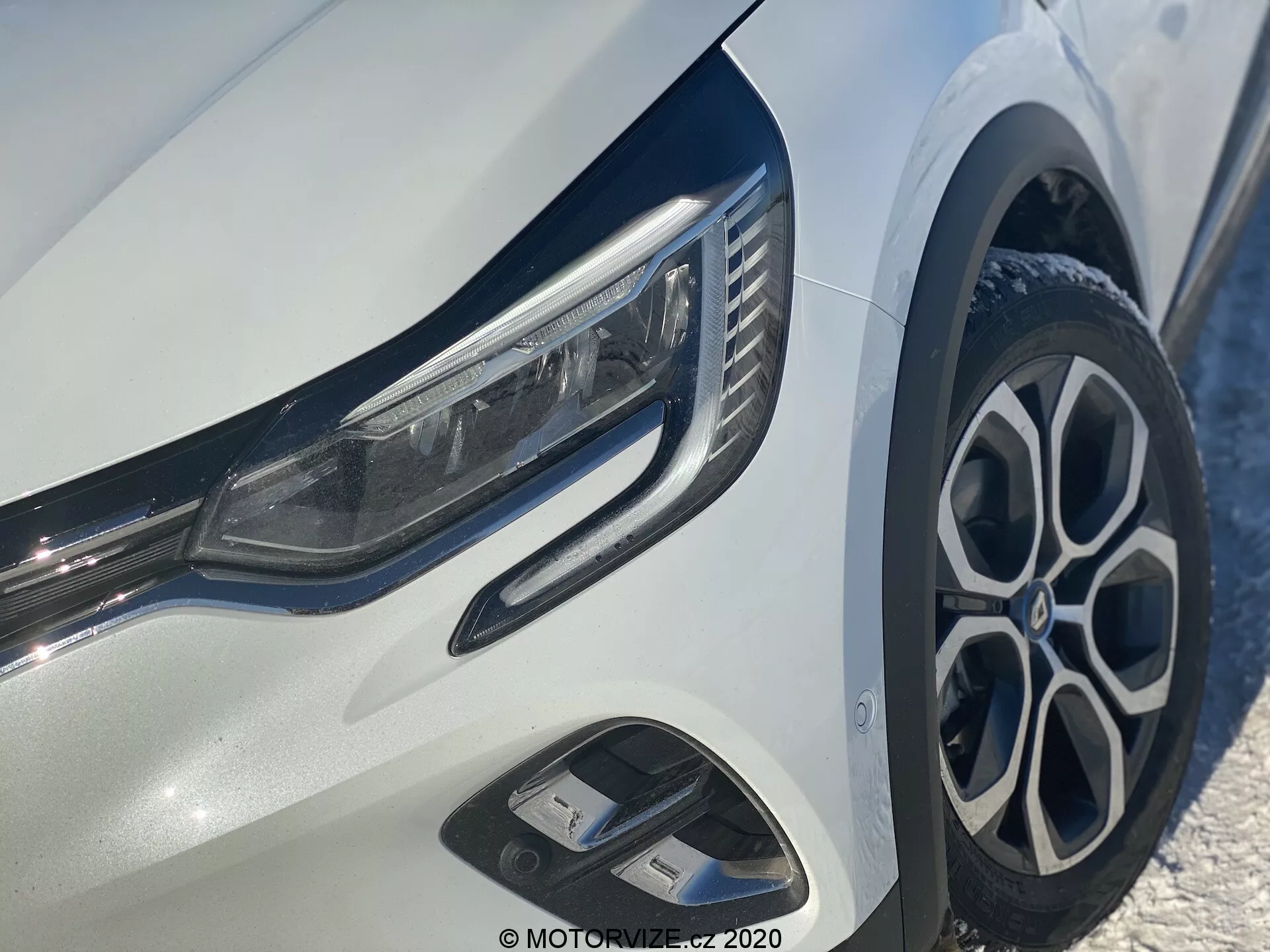 Närbild av Renault Captur 2020, fokuserad på vänster främre kvart, som visar eleganta LED-strålkastare, stilfulla flerspokes aluminiumfälgar, dynamisk främre stötfångare med luftintag och glänsande kromdetaljer på en ljus vit kaross.