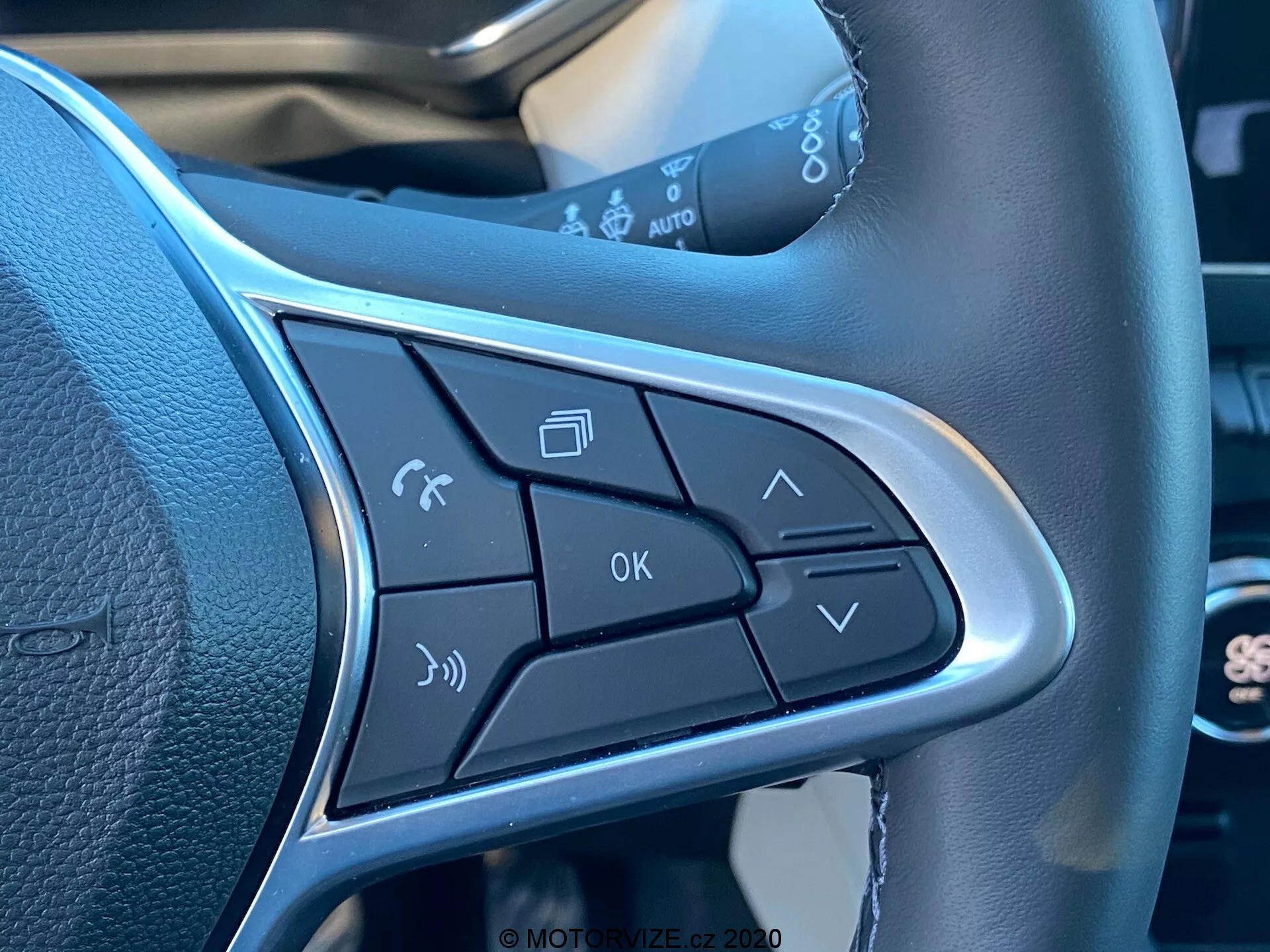 Närbild av kontrollknapparna på ekern på en Renault Captur 2020 ratt. Funktioner inkluderar aktivering av röstkommandon, hantering av telefonsamtal, volymkontroller, OK-knapp och meny-navigeringspilar. Den eleganta utformningen inkluderar en silverkant som framhäver knapparna och betonar handsfree-drift och bekvämlighet.
