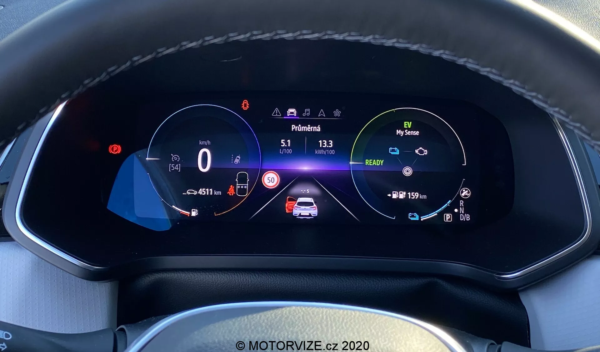 Närbild på Renault Captur 2020:s moderna bilens digitala instrumentpanel från förarens perspektiv. Den helt digitala högupplösta färgskärmen, monterad i en texturerad instrumentpanel med synliga sömmar, visar en hastighetsmätare på 0 km/h med en hastighetsgräns på 50 km/h, en central animerad bilgrafik med säkerhetsvarningar och batteriindikatorer, en varvräknare med ikonen för det miljövänliga läget 'My Sense', vägmätaravläsningar, utetemperatur och växelvisning i 'Park', samt ikoner för filhållningsassistans, automatiska helljus och adaptiv farthållare, allt i en välorganiserad layout som lyfter fram avancerad bilteknik och interiördesign.