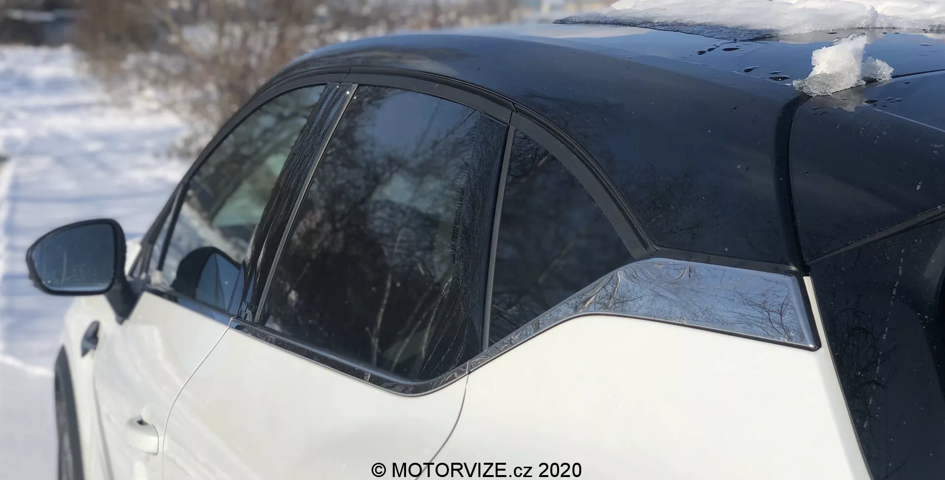 Sido vy Renault Captur 2020 i en vintermiljö, med en svart och vit tvåfärgad lackering. Bilden fokuserar på B-stolpen, en del av bakdörren och baksidan, fotad från en något bakre vinkel. Snöfläckar på taket och smältande is på fönstret reflekterar en ljus dag.