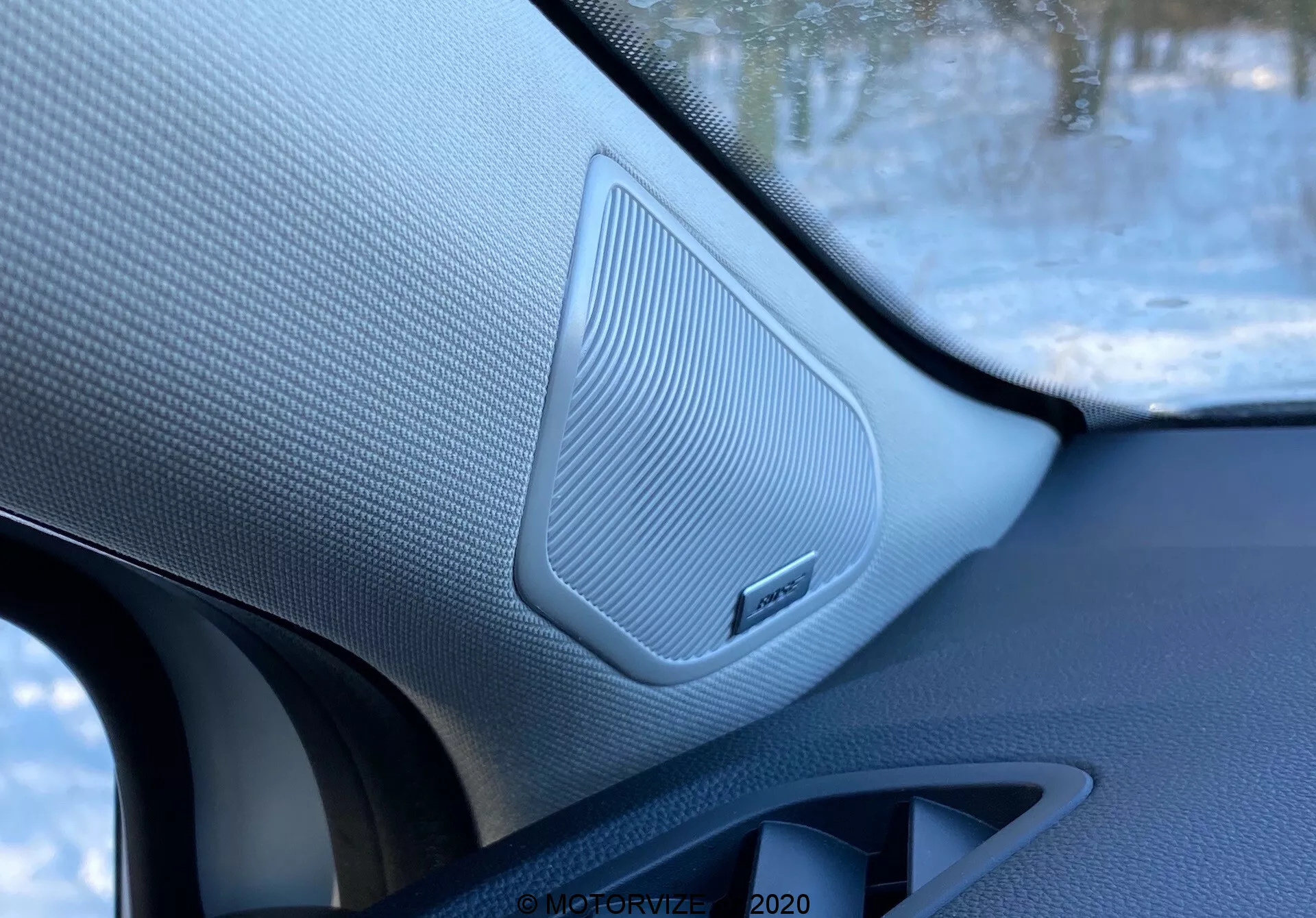 Närbild av interiören i en 2020 Renault Captur, som framhäver en högtalare på passagerarsidans framdörr med texturerat galler och varumärke, omgiven av kontrasterande material, tagen från fordonets insida.