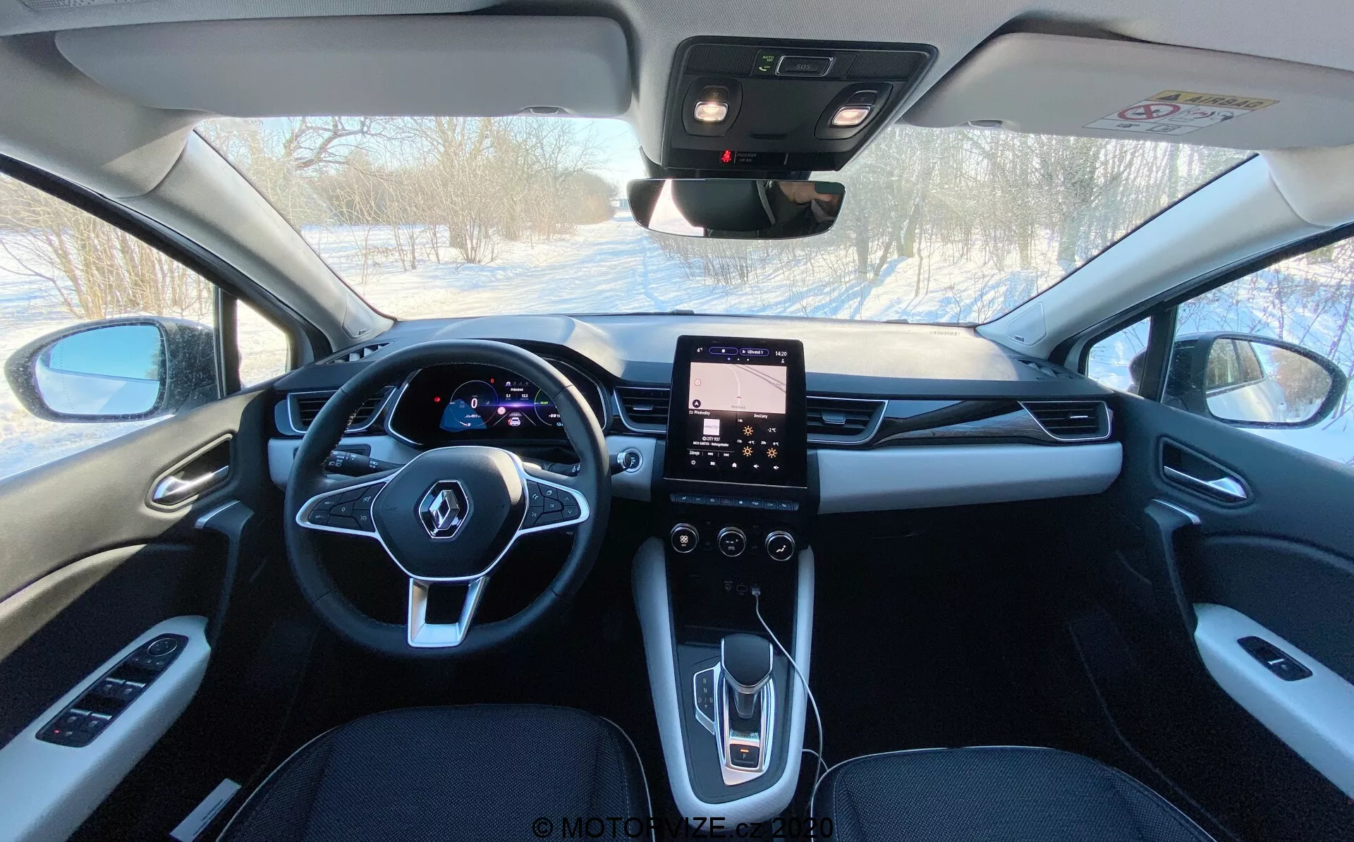 Interiörvy av en Renault Captur 2020 från baksätet framåt, som visar dess mörkfärgade klädsel, centrala backspegel, upplyst digital instrumentbräda bakom multifunktionsratten, pekskärmsinfotainmentsystem i mittkonsolen och reglage för elhissar, sidospeglar, klimatkontroll och troligtvis soltak samt nöd-SOS-knapp.