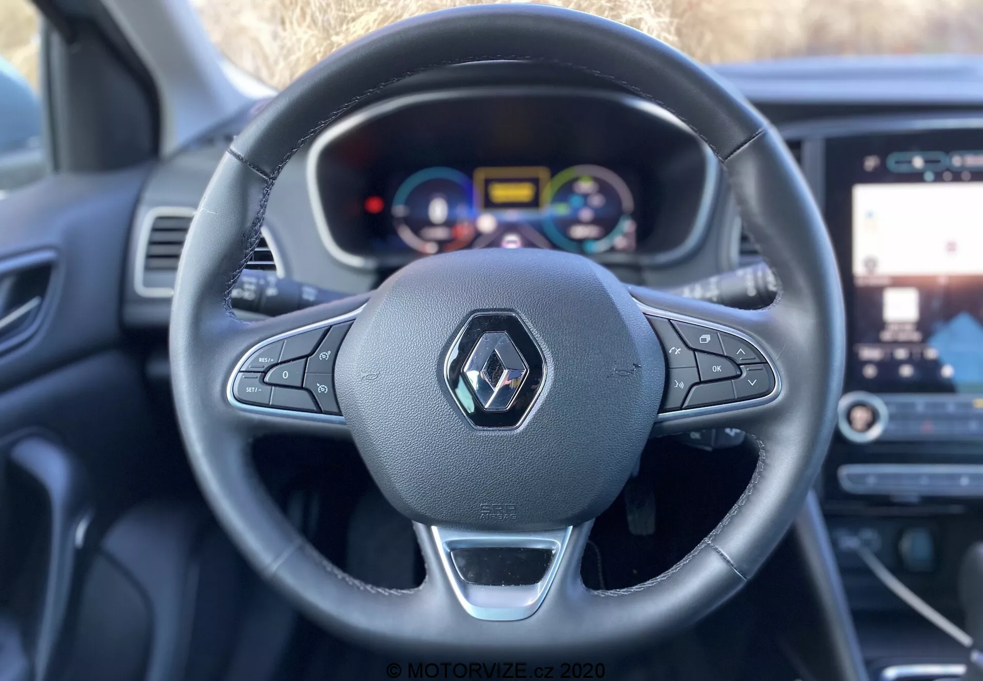Interiörvy av 2022 Renault Megane E-Tech från förarsätet, som visar en tre-ekrad ratt med monterade kontroller och metallisk accent, ett anpassningsbart digitalt instrumentkluster med färgglada mätare och förarassistansindikatorer, en glimt av infotainmentsystemets pekskärm med karta/navigationsdisplay samt en modern, ergonomisk interiördesign med material av läderliknande material och syntetiska material, tagen från förarens ögonperspektiv med kort skärpedjup som framhäver ratten och instrumentbrädan.