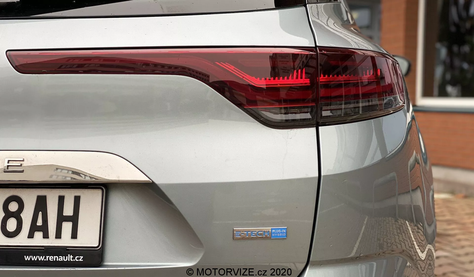 Vy över bakre hörnet av en metallisk silver Renault Megane 2022 E-TECH, som visar det högra bakljuset med moderna LED-ljuselement och E-TECH-märket på bakersta bagageluckan. Den bakre stötfångaren och delvis hjulbåge syns också, vilket indikerar bilens hybrid- eller eldrivlina.
