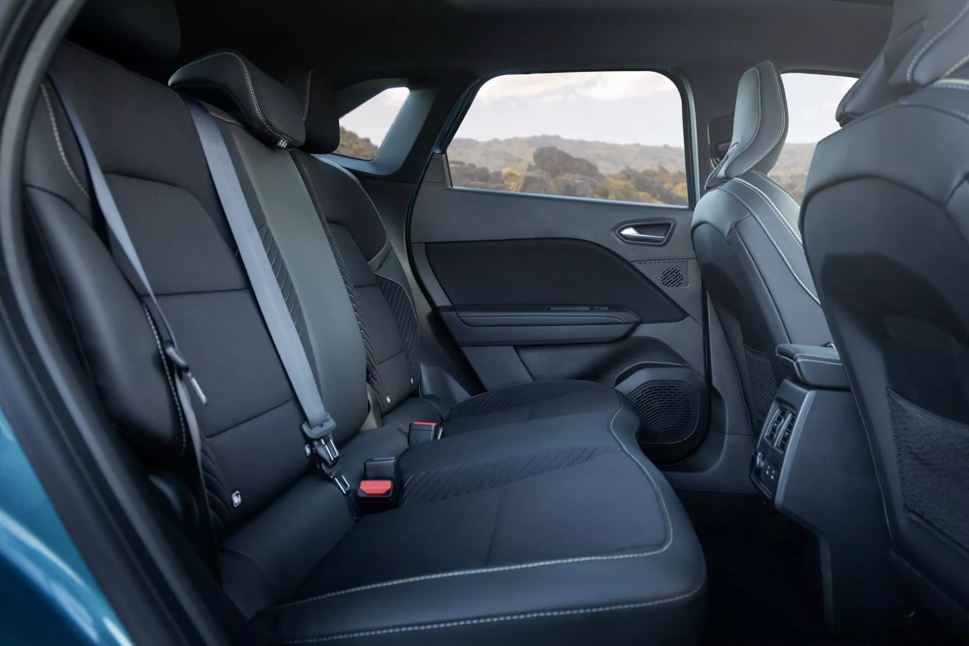 Interiörvy av Renault Symbioz 2024 (1:a generationen) som visar bakre sätesområdet i svart läder med vita sömmar, framhäver den konturerade 2+1 säteskonfigurationen samt elegansen och komforten riktad mot modern bildesign. Synlig dörrpanel med högtalargaller och armstöd, med standard trepunktsbälten.