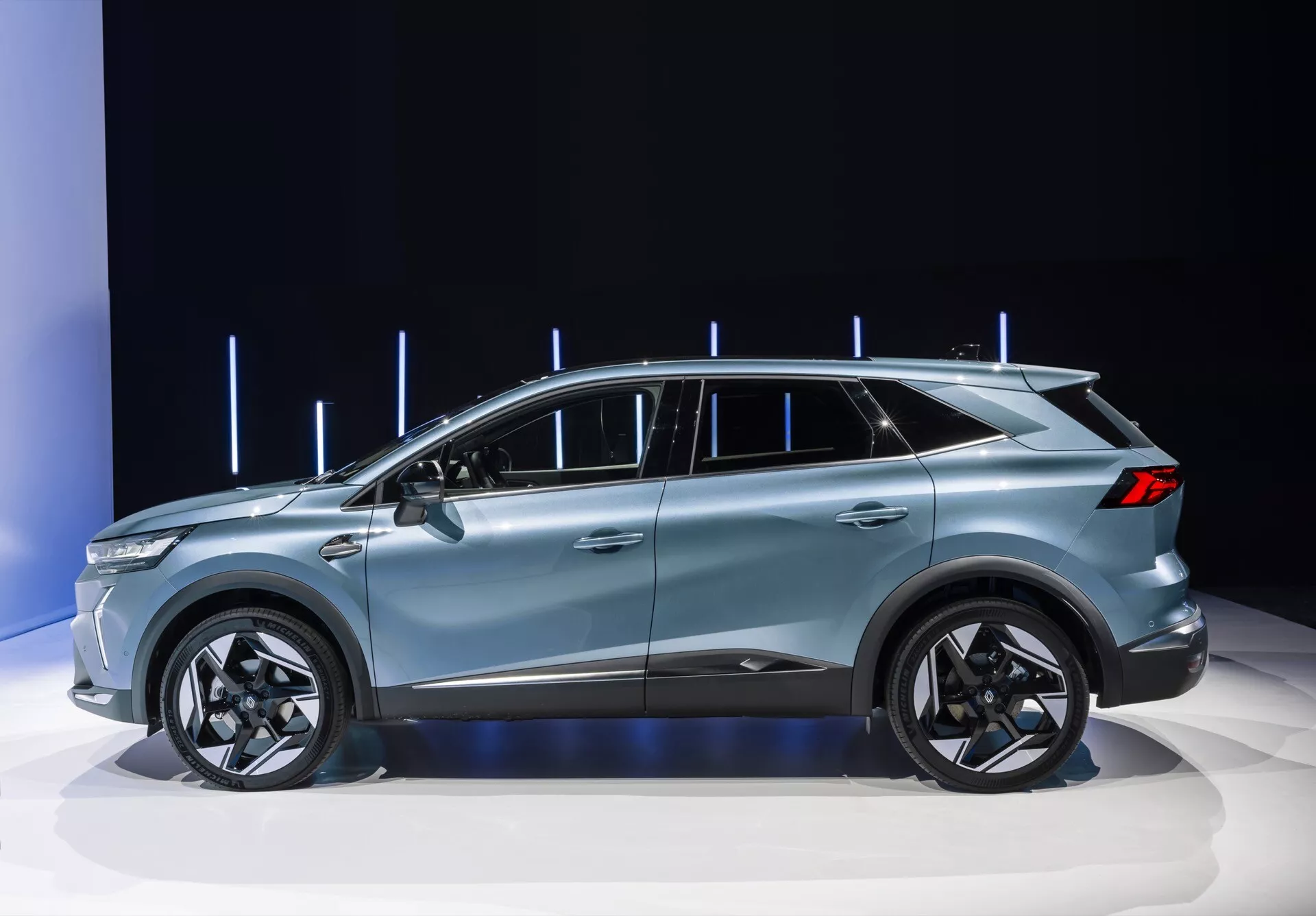 Bildet visar Renault Symbioz 2024 (första generationen) som ställs ut på en bilmässa, tydligt framhäver den eleganta sidprofilen av den moderna crossover-SUV:en. Fordonet har ett tak med coupé-liknande linjer, femdörrars konfiguration, stora legeringshjul och sofistikerade designlinjer, allt framhävt av en ren, välbelyst bakgrund med vertikala ljuselement. Designen antyder premiumfunktioner som LED-teknik, aerodynamisk effektivitet och möjligen avancerade förarassistanssystem.