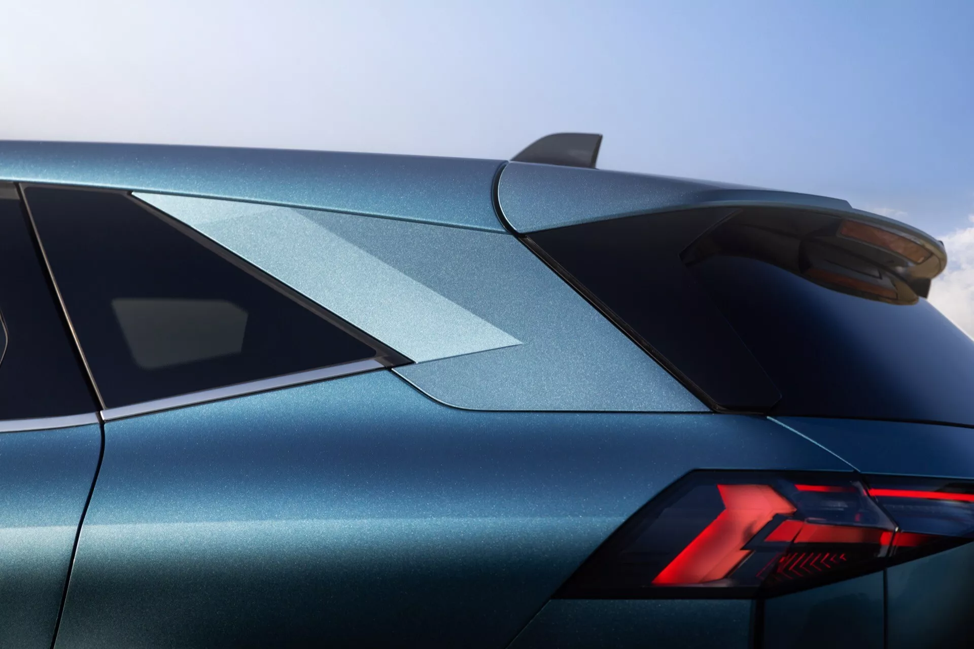 Trebild av den bakre tre fjärdedelar av 2024 års Renault Symbioz, som fokuserar på den övre bakdelen. Bilden visar en distinktivt stylad bakljus med moderna LED-element i en 'Y'-konfiguration. Den eleganta karossen, utförd i en skimrande metallisk blågrå färg, visar skarpa, definierade karaktärslinjer. Den brant lutade bakrutan och monterade bakspoilen framhäver bilens sportiga estetik. En hajfensantenn är synlig på taket, vilket ytterligare indikerar moderna designinslag. Den höga byggkvaliteten och exakta detaljerna är påtagliga från denna vinkel, vilket tyder på en lyxig eller prestandainriktad fordon.