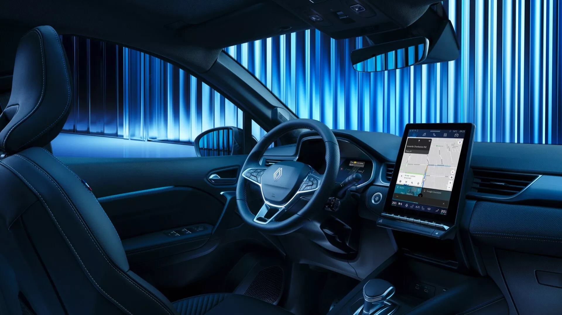Vy från baksätet på interiören i Renault Symbioz 2024, med centralt placerad ratt med integrerade kontrollknappar, en digital instrumentpanel och en framträdande porträttorienterad infotainmentskärm som visar en karta. Kupén har en blå nyans av ambient belysning, vilket tyder på en modern och teknikorienterad design, minimala fysiska knappar på mittkonsolen och en del av dörrpanelen med ett integrerat högtalargaller, vilket indikerar ett premiums ljudsystem.