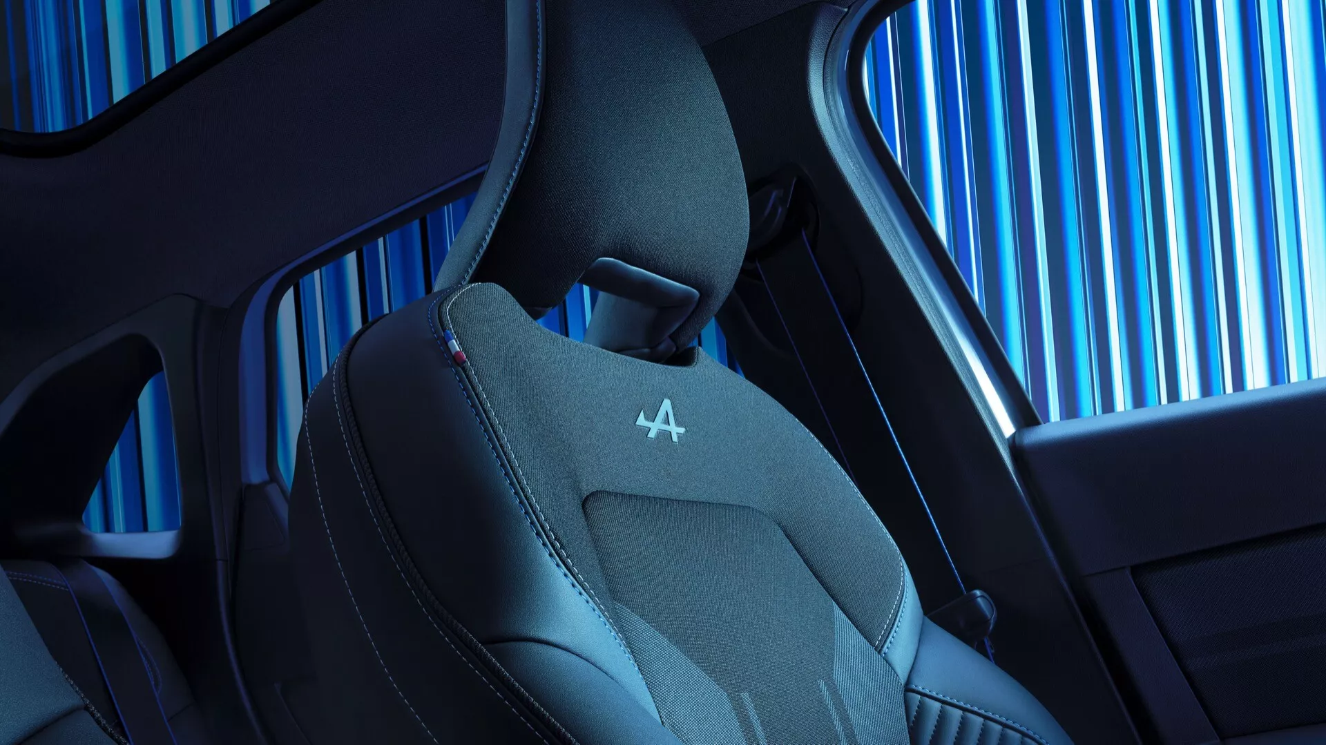 Närbild av interiören i 2024 års Renault Symbioz första generationen, som betonar modern design och tekniska funktioner. Visar överdelen av sätet med ergonomisk form, konturerade sidostöd och en blandning av läder och andningsbart tyg för lyx och komfort. Noterbara röda sömmar på nackstödet med präglad logotyp, tillsammans med en glimt av bilens sidofönster och elegant kabindesign.
