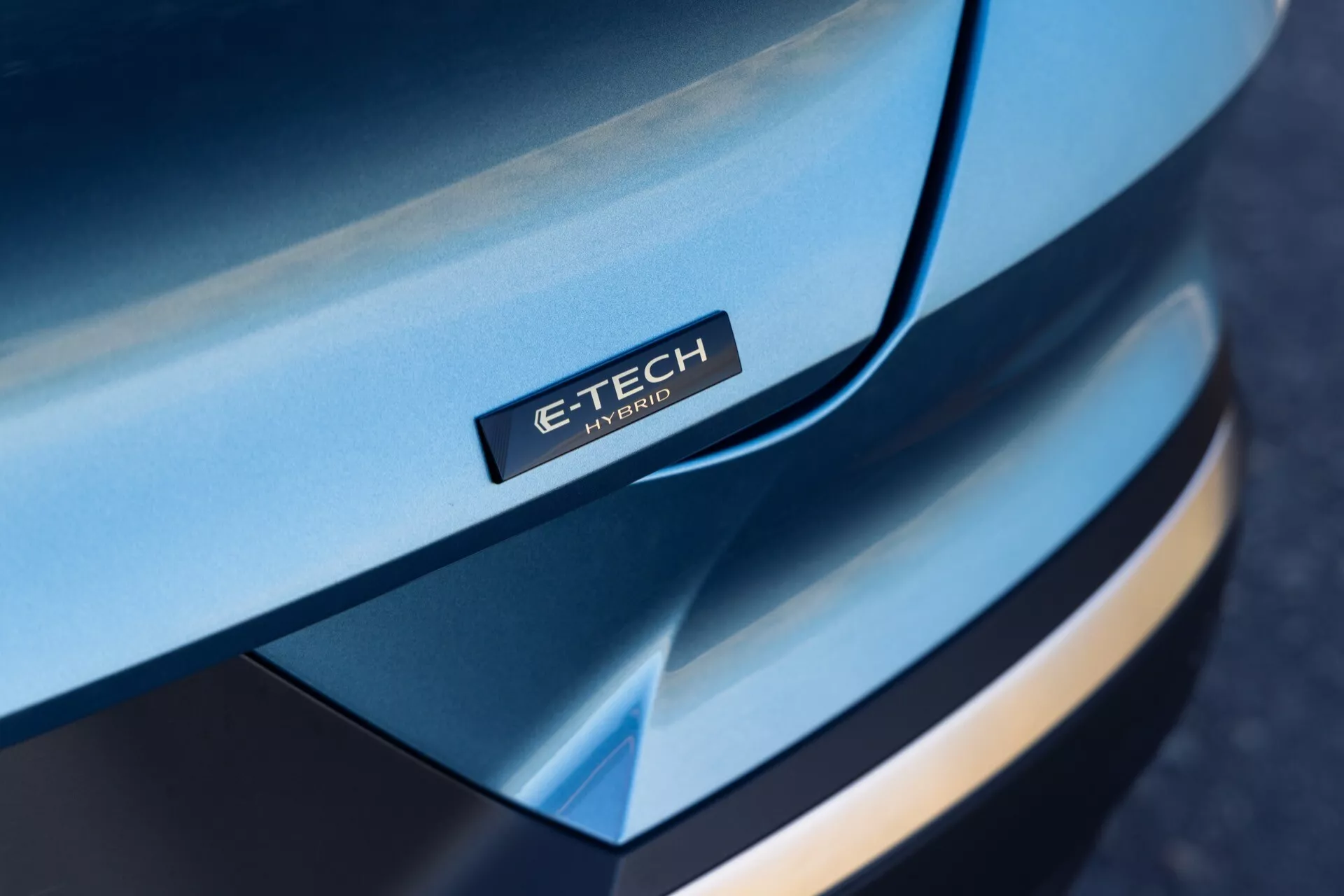 Närbild i vinkel av främre delen av Renault Symbioz 2024, med fokus på den eleganta, välvda huven med märket 'E-TECH Hybrid', mångskiktsdesign på främre stötfångaren, kontrasterande färger och premium-utseende, som framhäver hybridteknologin.