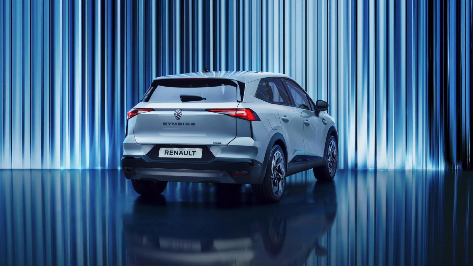 Denna professionella bild visar bakänden av första generationens 2024 Renault Symbioz, en samtida SUV-modell. Fordonet har distinkta LED-bakljus, en bakspoiler, en bakre vindrutetorkare, Renault-emblemet och modellnamnet. Lågkameravinkeln framhäver dess hållning och betonar den rena designen utan synligt avgasrör, vilket indikerar en hybrid- eller eldrift. Mot en livfull bakgrund med vertikala blå ljusstrimmor, skapar bilens ljusa metallicfärg och den reflekterande polerade golvet en sofistikerad showroom- eller iscensatt fotosession-atmosfär.