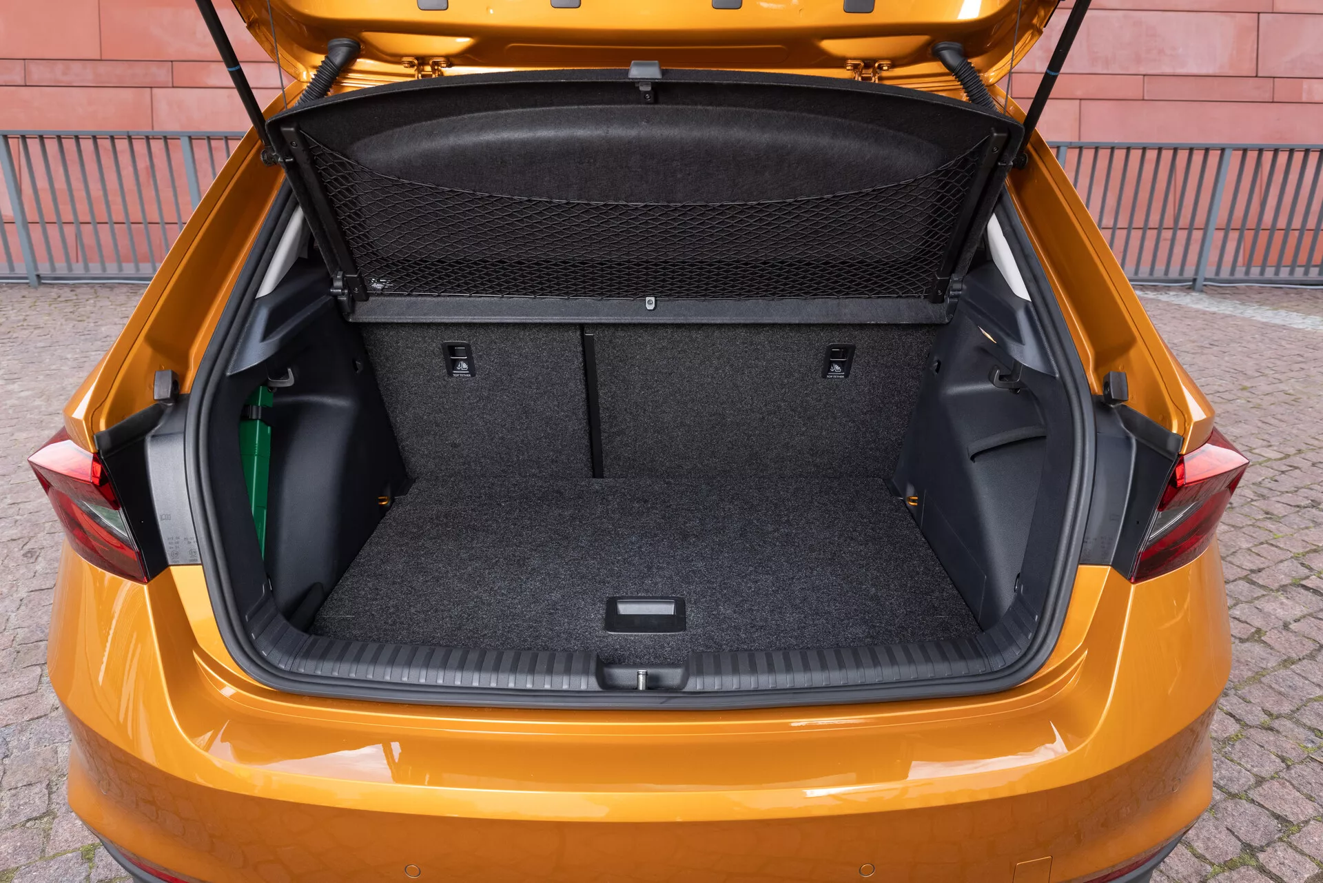 Bilden visar bagageutrymmet på en Skoda Fabia 2021, fotograferat från en något upphöjd vinkel bakifrån för att visa det rymliga lastutrymmet. Interiören är fodrad med ett matta-liknande material och har flexibla sidoförvaringsområden, ett bagagenät och en nedsänkt del på botten för extra förvaring. Bakluckan är upplyft, vilket avslöjar ett stort rent bagageutrymme, designat för att framhäva fordonets lastkapacitet och praktiska egenskaper.