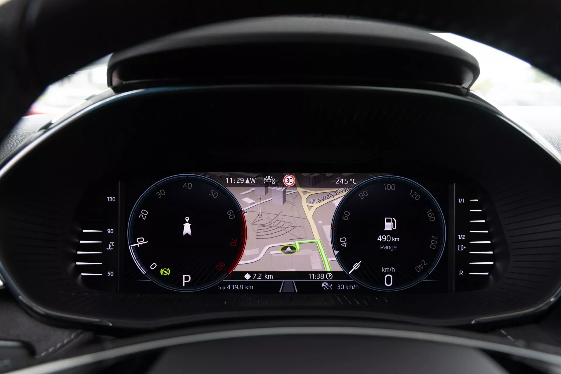 Närbild av 2021 års Skoda Fabias moderna instrumentkluster från förarens perspektiv, med analog hastighetsmätare, stor digital display med navigationskarta och digital varvräknare. Displayerna visar 23:29, 24,5°C, en räckvidd på 490 km, aktuell hastighet på 0 km/h och reseinformation. Kombinerar traditionell och modern design med avancerad teknik inklusive realtidsnavigering, förarinformation och anslutningsindikatorer.