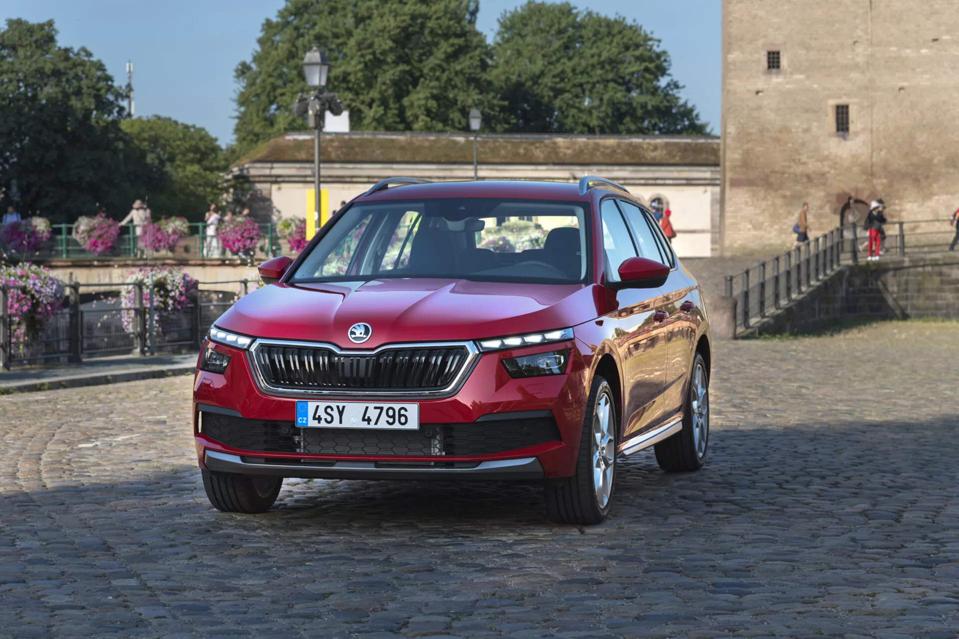 2019 Skoda Kamiq i djupt metalliskt rött, som visar designfunktioner som grill, LED-strålkastare och legeringshjul på en kullersten stadsbakgrund