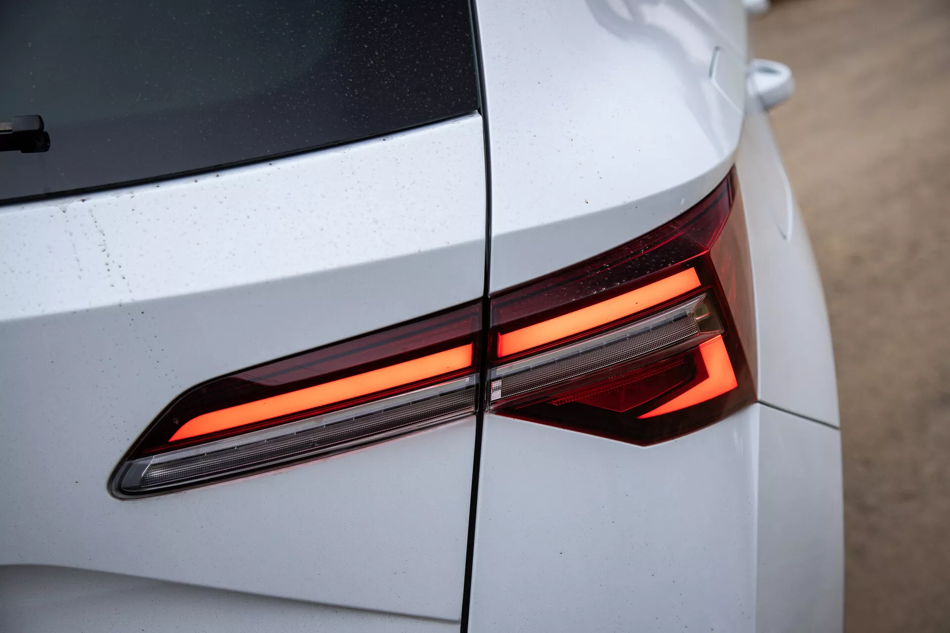 Närbild av Skoda Karoq 2021s baksektion som visar den moderna LED-bakljusdesignen, med betoning på de vinklade linjerna och den glansiga, ljusfärgade karossen med synliga vattendroppar