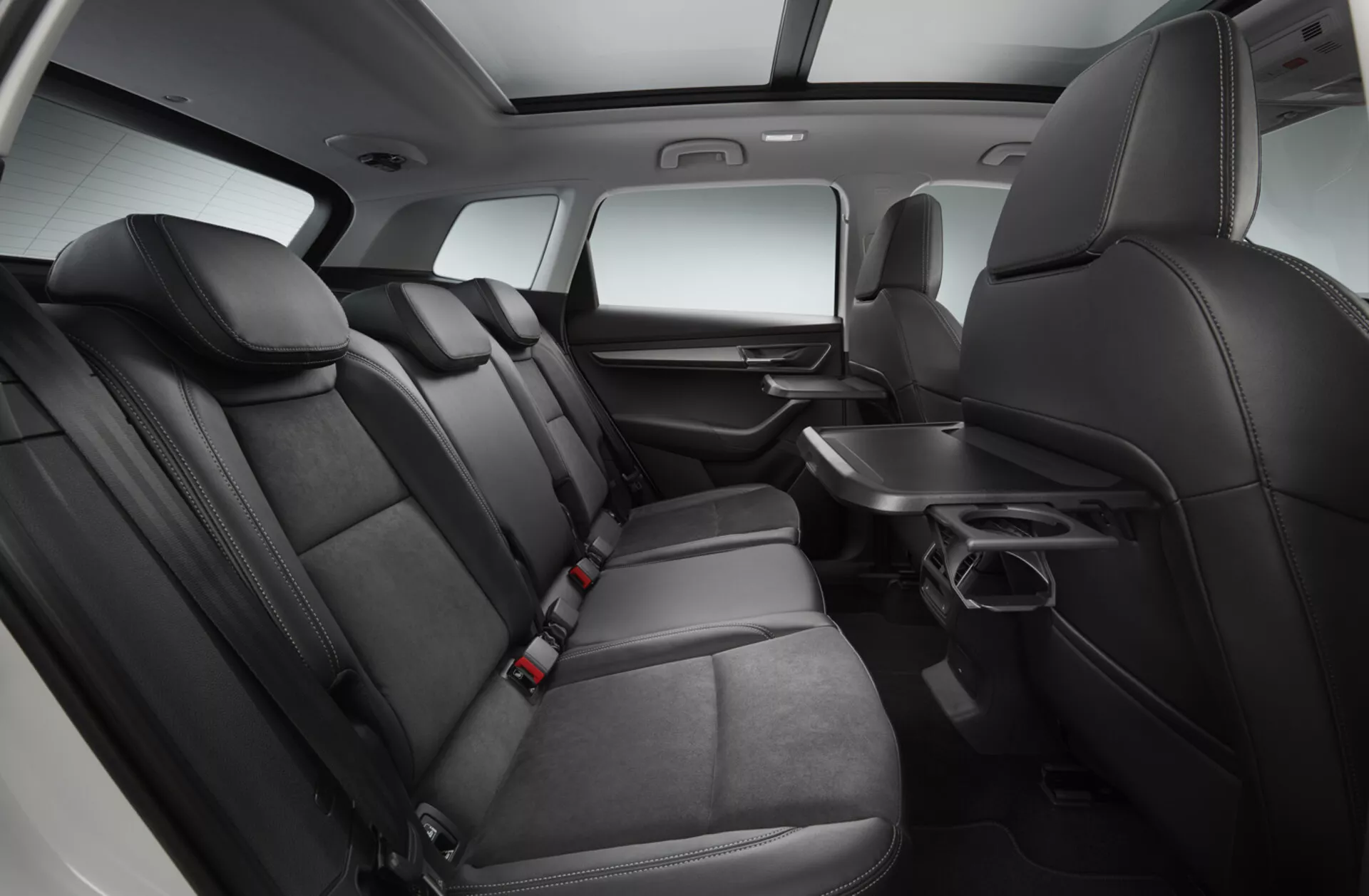 Interiörvy av en Skoda Karoq 2017 med fokus på andra radens sittplatsområde med premium svarta lädersäten, fällbart armstöd med mugghållare, dörrpanel med elkontroller, förvaringsfickor bakom första radens säten, säkerhetsbälten för alla platser och en mittpanel som sträcker sig till andra raden, allt under förbättrad studiobelysning