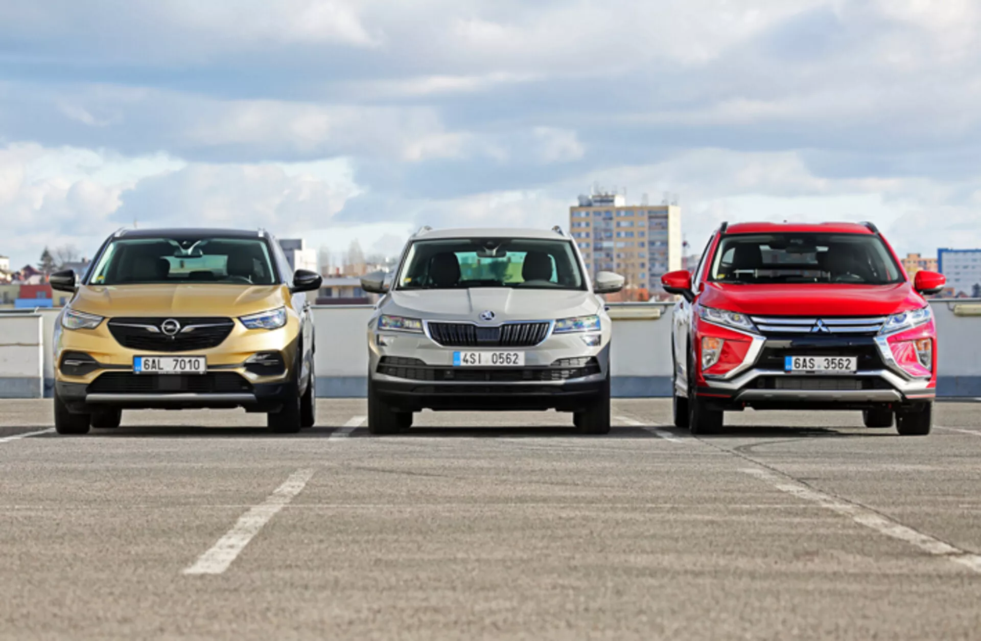 Framifrån vy av tre Skoda Karoq 2017 modeller på en parkeringsplats med stadssilhuett i bakgrunden, som visar olika grill-, strålkastar designer och aerodynamiska huvar under molniga dagljusförhållanden