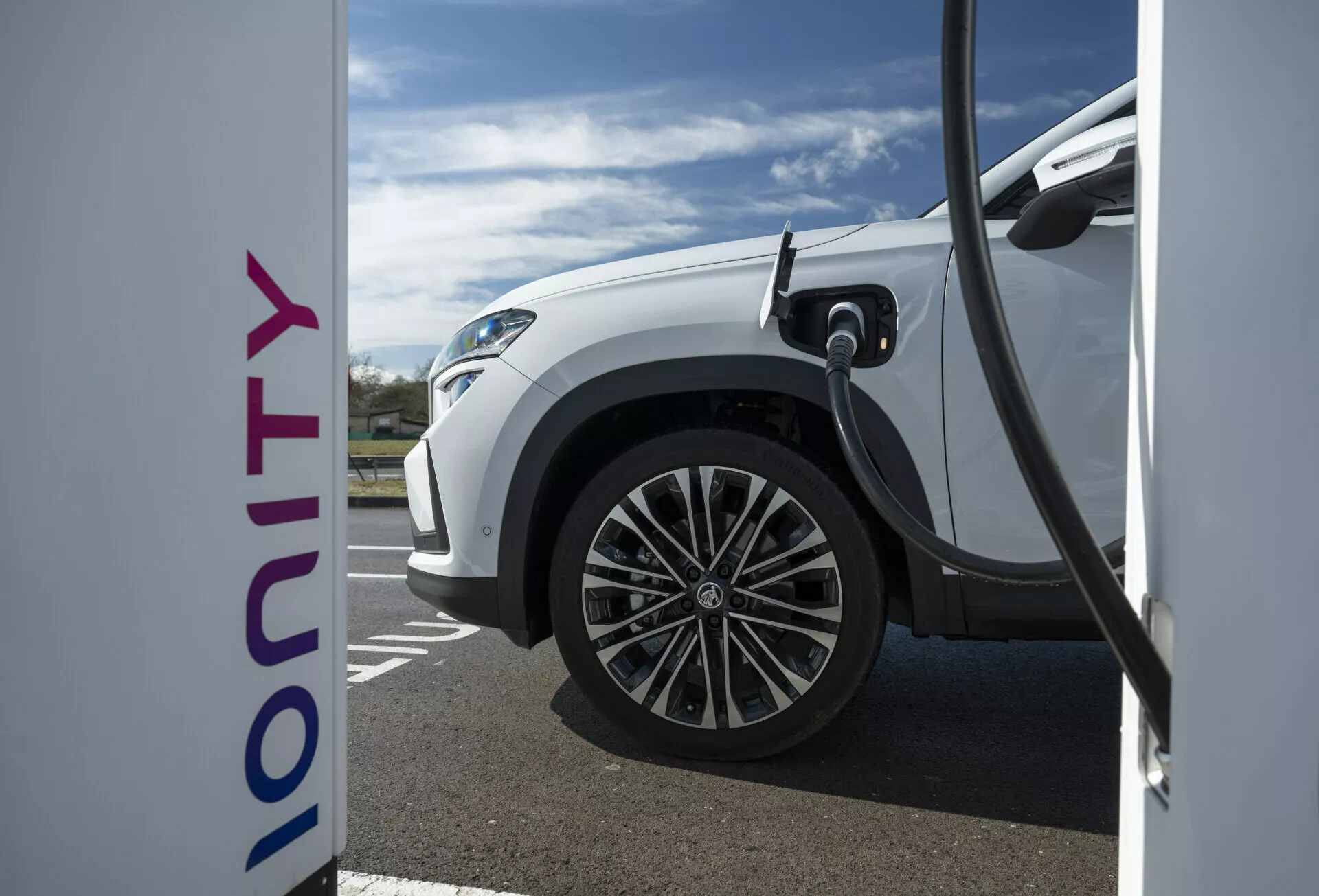 Närbild på sidovy av en vit 2024 Škoda Kodiaq elektrisk bil som laddas vid en Ionity-station, vilket visar snabbladdningsteknik och modern design