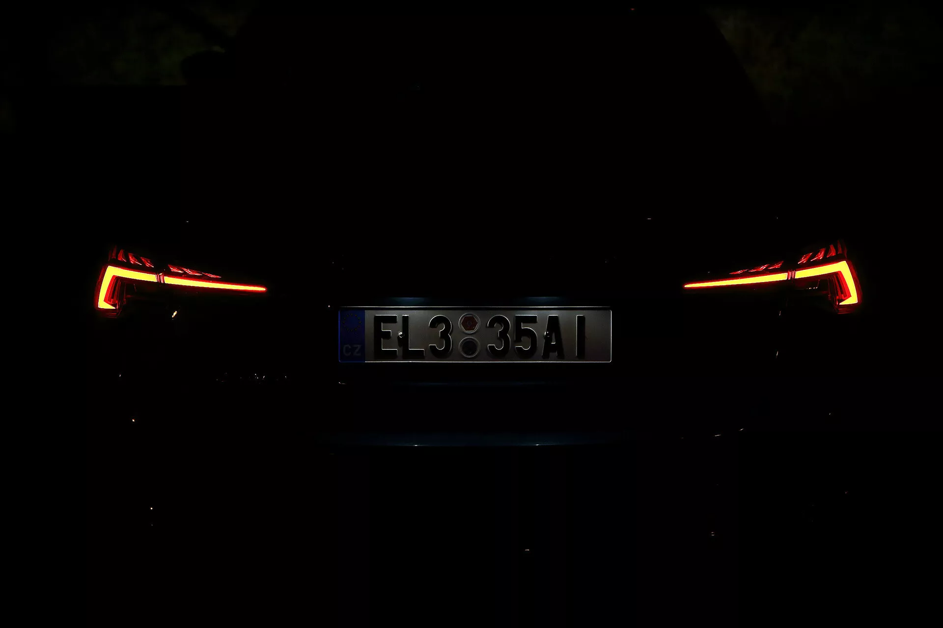 Bakifrån perspektiv av en Skoda Octavia 2020 Limousine, fotograferad på natten eller i en svagt upplyst miljö. Bilden fokuserar på de upplysta bakljusen och registreringsskylten, som visar en modern och kantig design. Bilens detaljer är dolda på grund av den svaga belysningen, vilket framhäver den eleganta och moderna baksektionen.