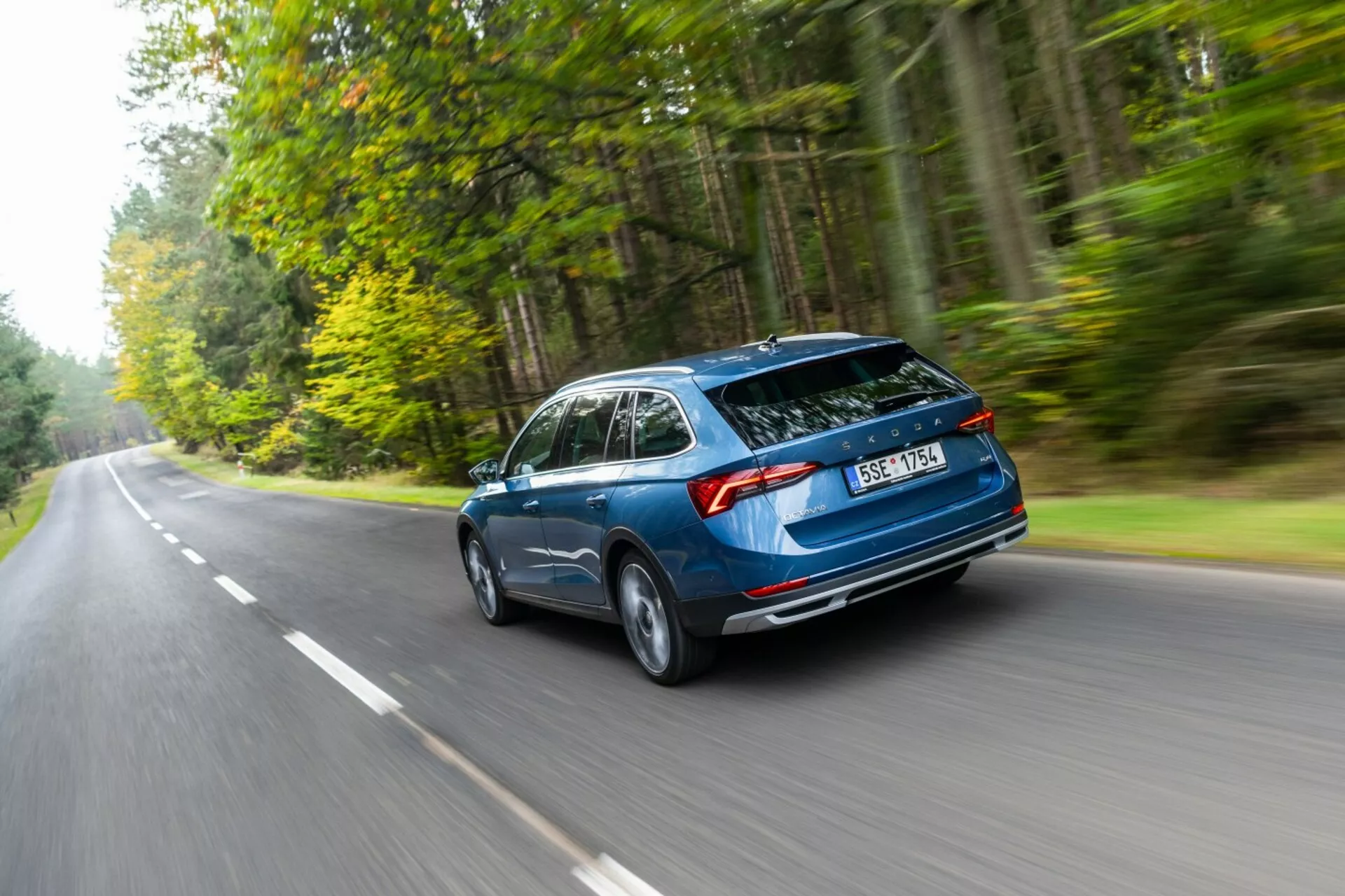 Skoda Octavia kombi från 2017 i rörelse, fångad från ett bakre tredjedels vinkel som framhäver aerodynamisk design, bakre hatchbackbagage och horisontella bakljus på en skogsbeklädd väg