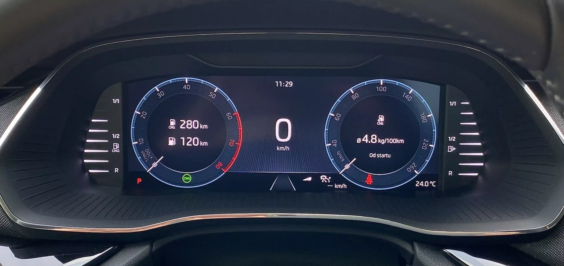 Närbild av Skoda Octavia 2020 digitala instrumentpanel ur förarens perspektiv, med en bredbildsskärm med svart bakgrund och livfull digital grafik. På vänster sida visas en varvräknare upp till 8 000 RPM med rödmarkering vid 6 500 RPM och nålen vid tomgång. I mitten visas en hastighet på '0 km/h', en klocka vid '11:29', bränsleförbrukning på '4,8 l/100km' och en distans på '6540 km'. På höger sida finns en grafik som liknar en hastighetsmätare med skalor upp till 280 km/h och en temperatur på '24°C'. Ikoner inkluderar en navigationskompass och en bränslenivåmätare.