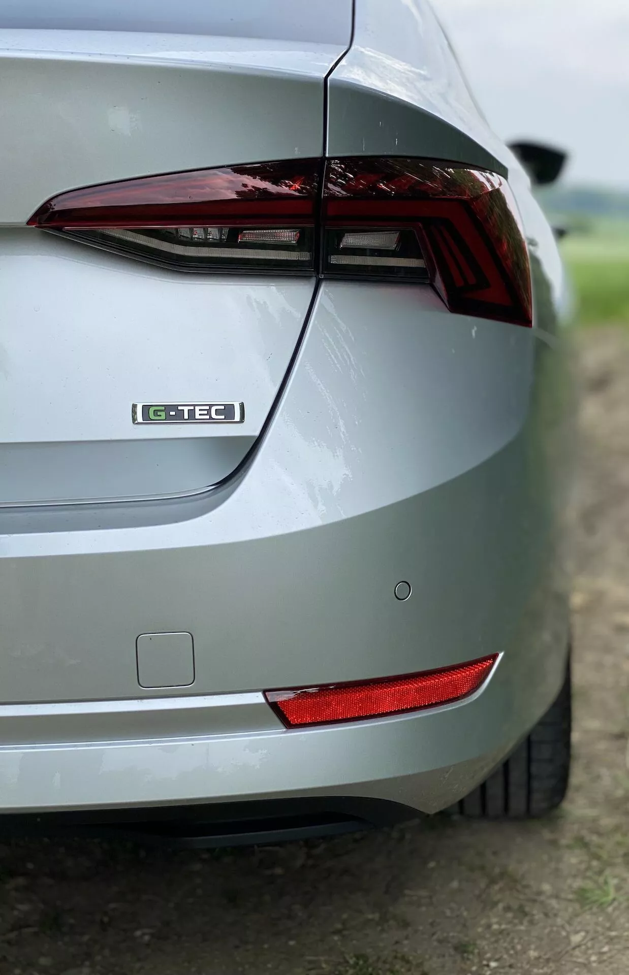 Närbild av högra bakre hörnet på en silverfärgad Skoda Octavia Limousine 2020 från sned vinkel. Bilden framhäver bakljus, G-TEC-märke, elegant bagagedesign, bakre stötfångare, bakre reflex och metallic färgfinish. Den suddiga bakgrunden betonar bilens designfunktioner.