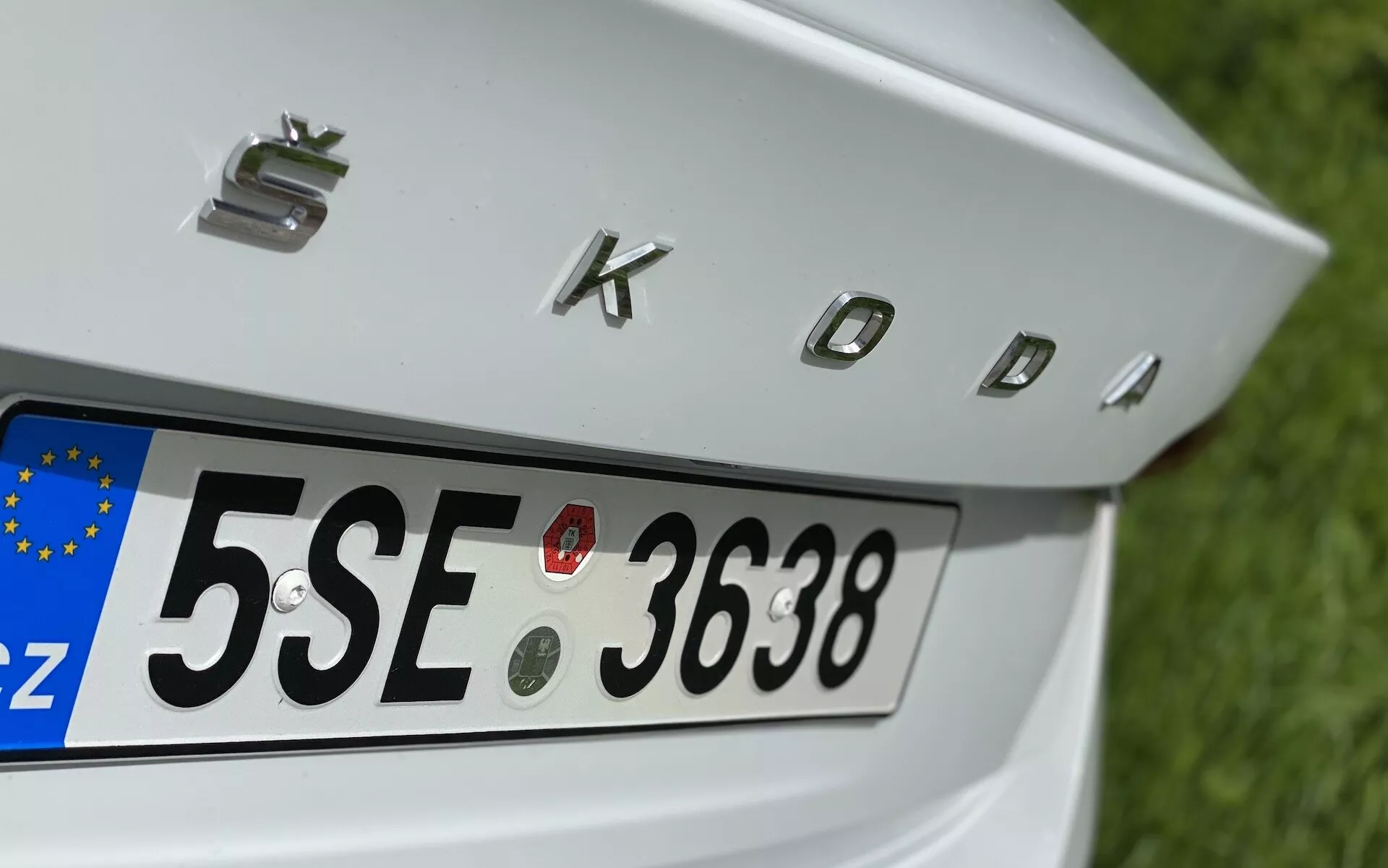 Närbild på bakre delen av Škoda Octavia 2020 limousine med fokus på bakluckan, bakre registreringsskylt med europeisk 'CZ' identifierare och kromade bokstäver 'SKODA'. Funktioner inkluderar fyra cirkulära parkeringssensorer ovanför registreringsskylten för att underlätta manövrering av fordonet.